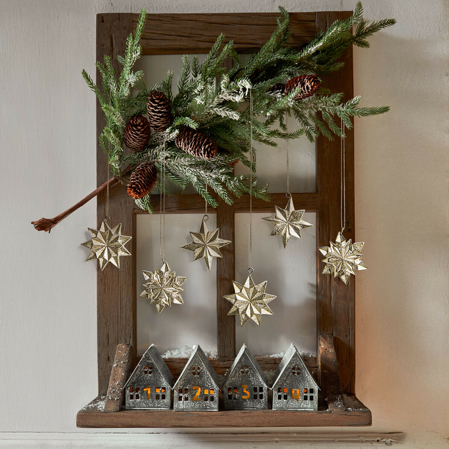 Set de 6 colgantes Zamoura Decoración navideña con casitas metálicas numeradas y estrellas doradas colgadas en marco de madera con rama de pino