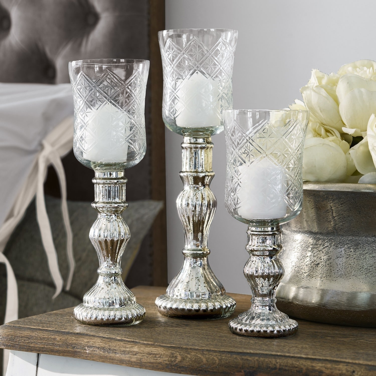 Conjunto de tres candelabros de vidrio con base metálica plateada sobre mesa de madera