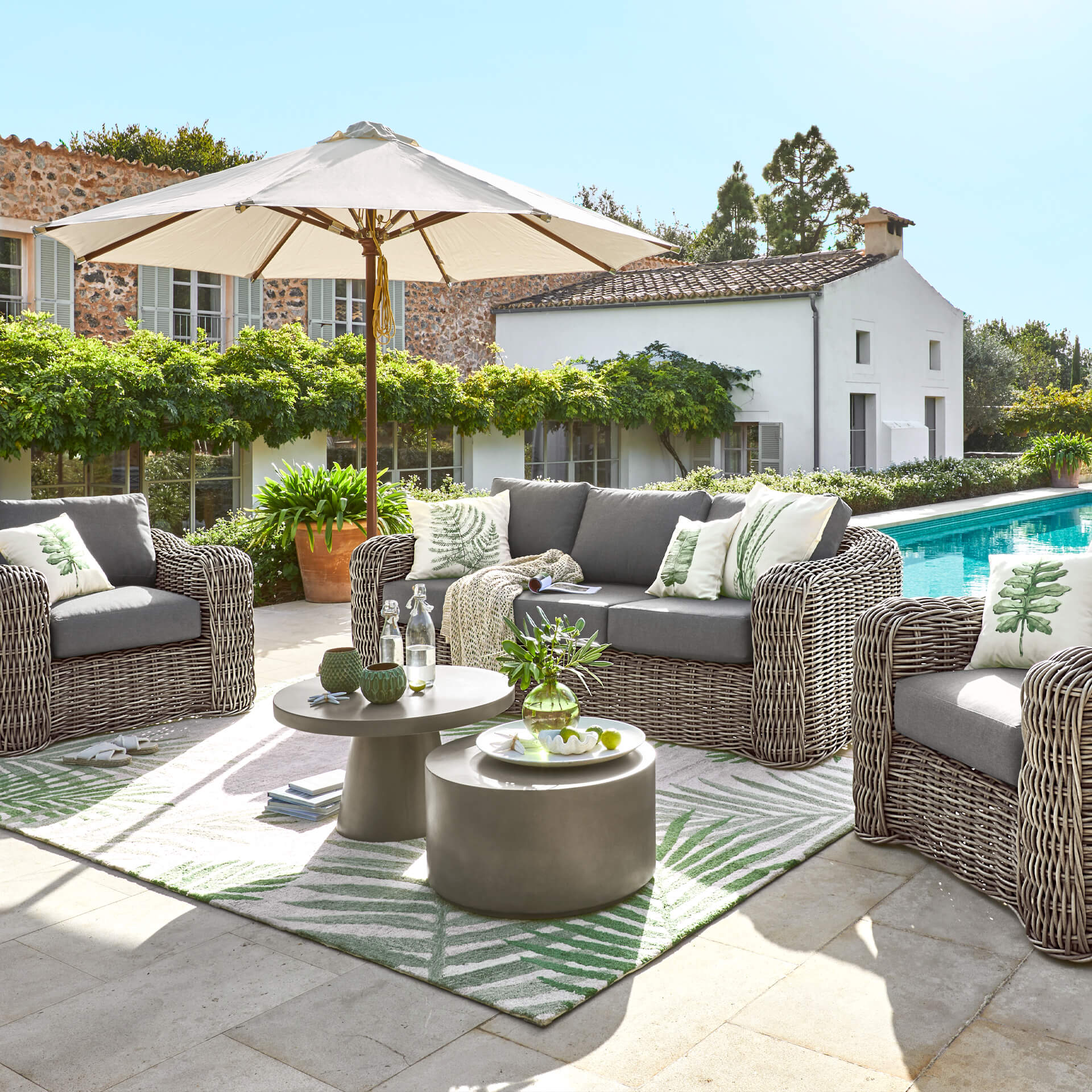 Conjunto de muebles de jardín de tecnoratán gris con cojines y sombrilla junto a la piscina