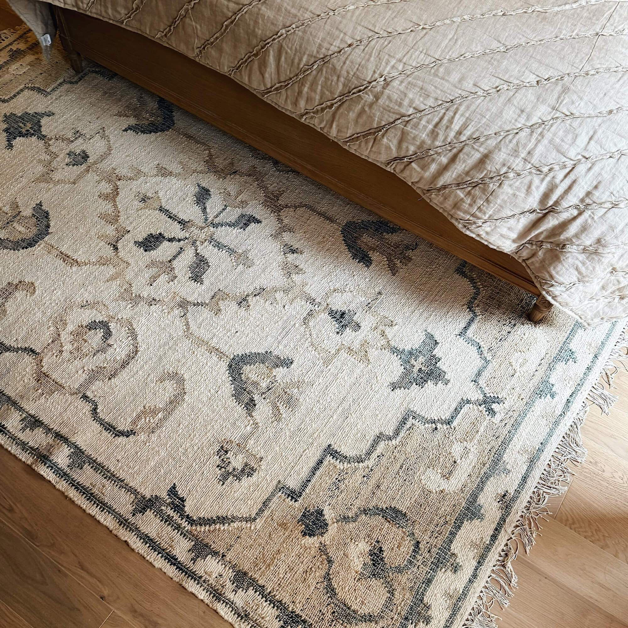 Alfombra beige con diseño oriental y flecos sobre suelo de madera junto a la cama