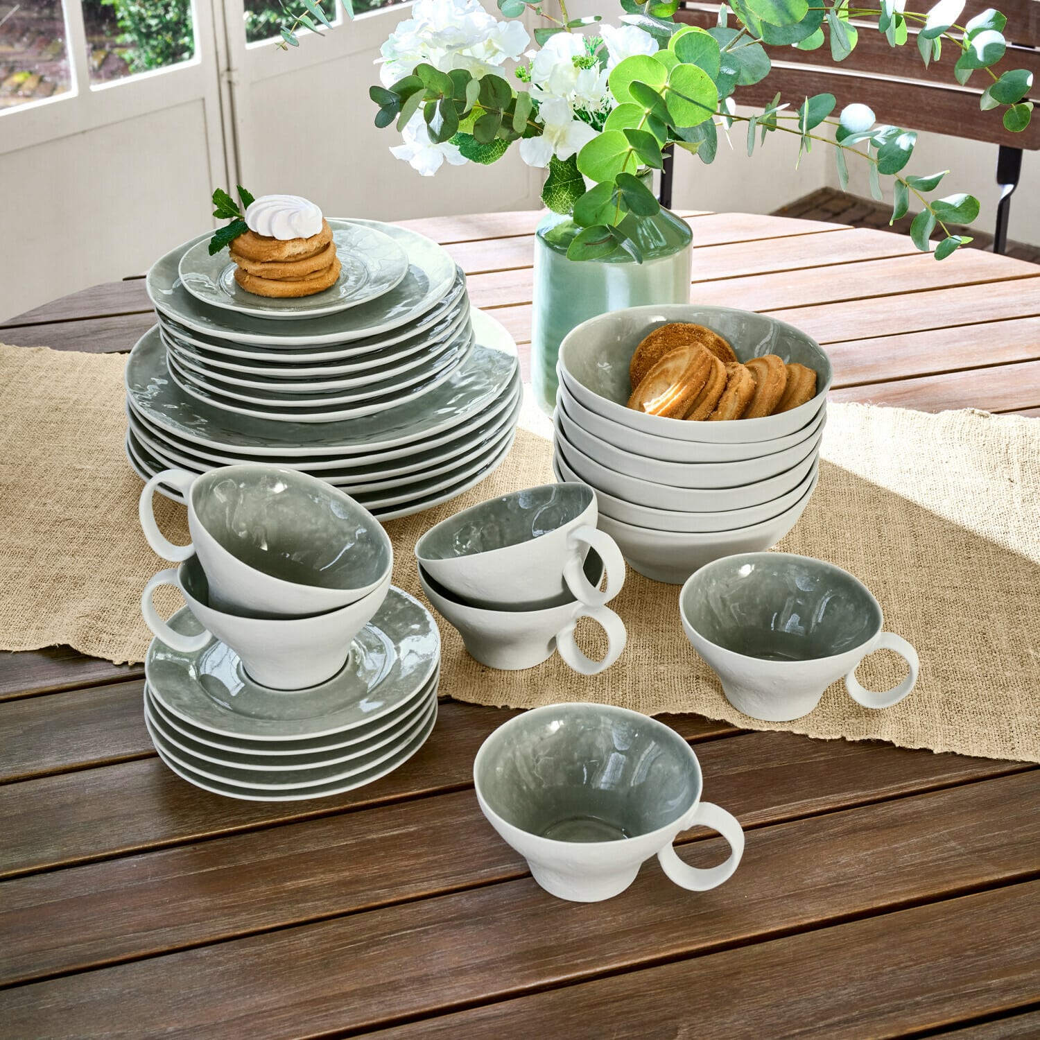 Set de 30 piezas de vajilla Braganza Juego de vajilla de cerámica gris y blanca sobre mesa de madera con galletas y flores decorativas