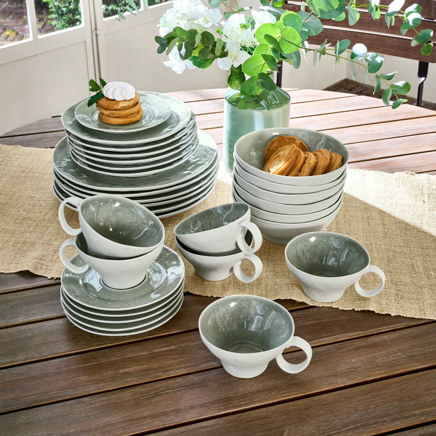 Set de 30 piezas de vajilla Braganza Juego de vajilla de cerámica gris y blanca sobre mesa de madera con galletas y flores decorativas