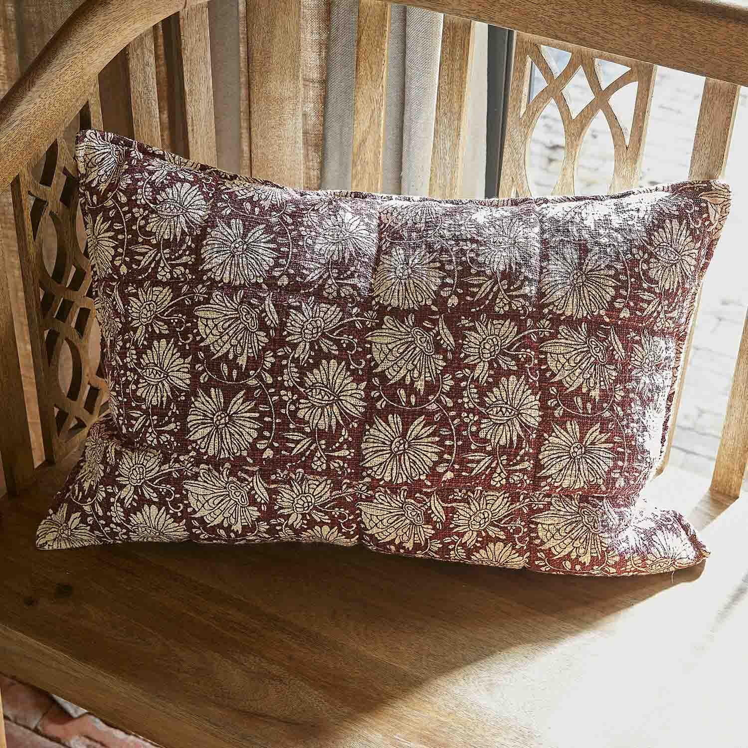 Cojín decorativo de algodón burdeos con diseño floral crema sobre banco de madera
