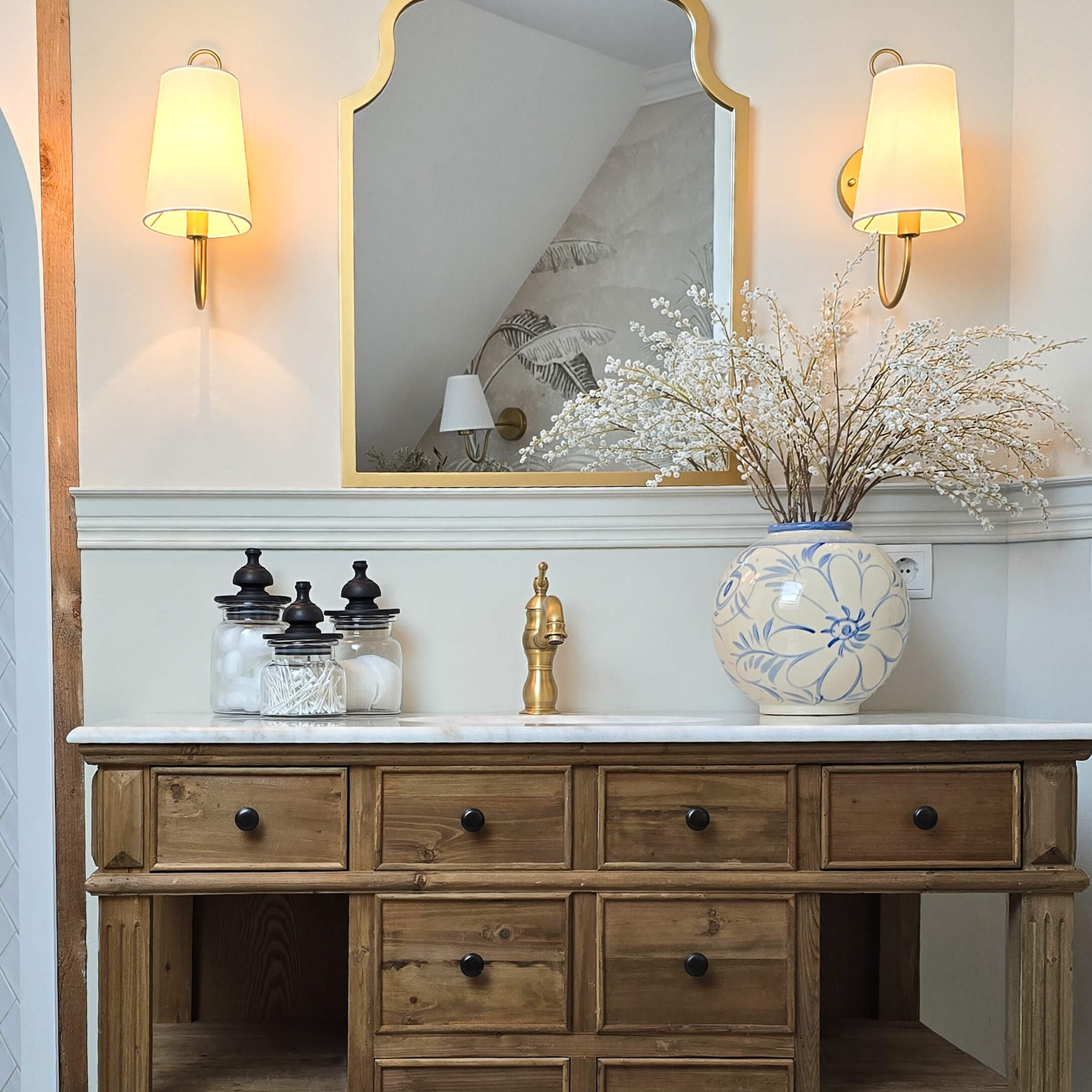 Cómoda de madera con encimera de mármol, grifo dorado y jarrón cerámico azul y blanco con flores