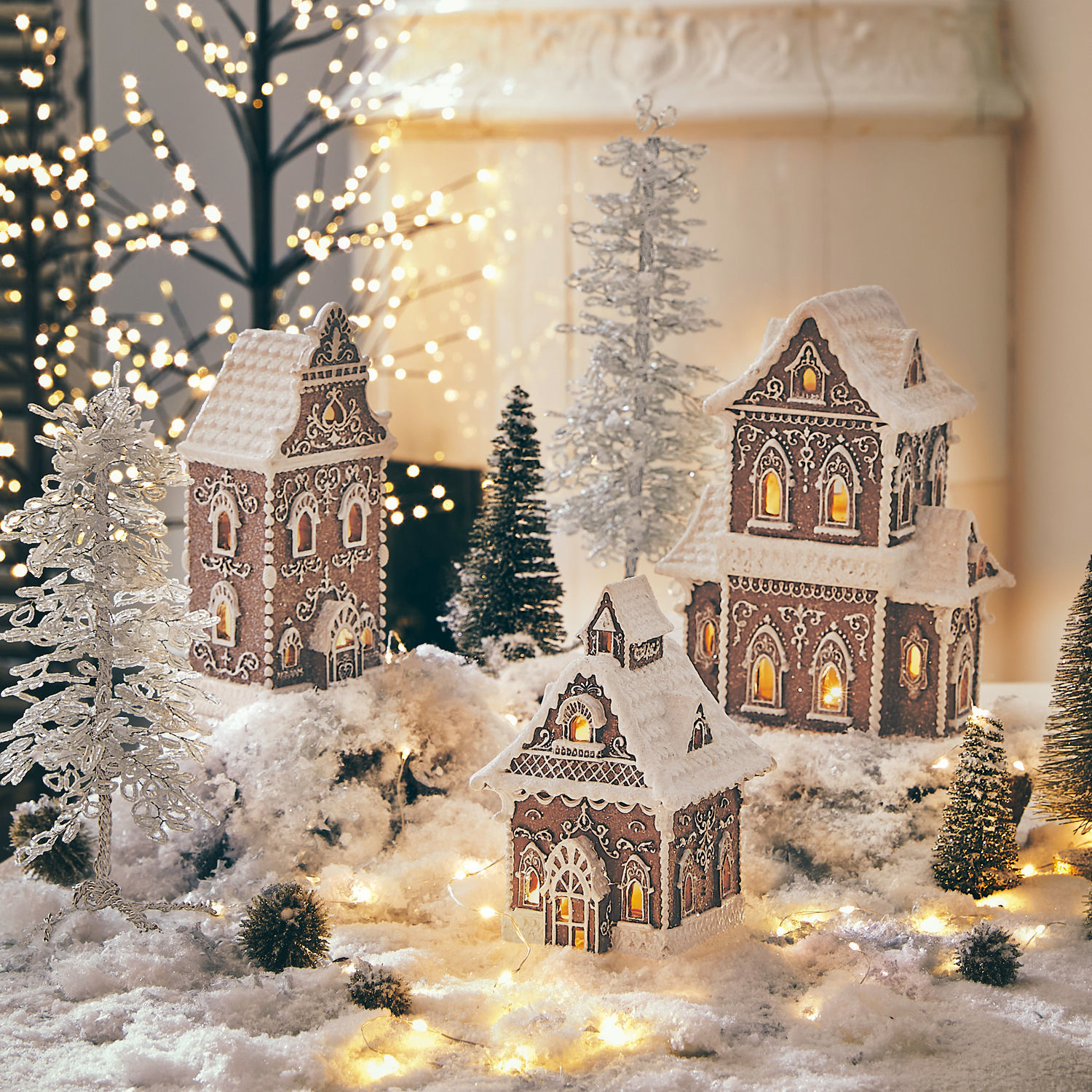 Set de 3 casitas decorativas Anyama Casitas de jengibre decorativas con glaseado blanco y luces sobre fondo nevado con pinos