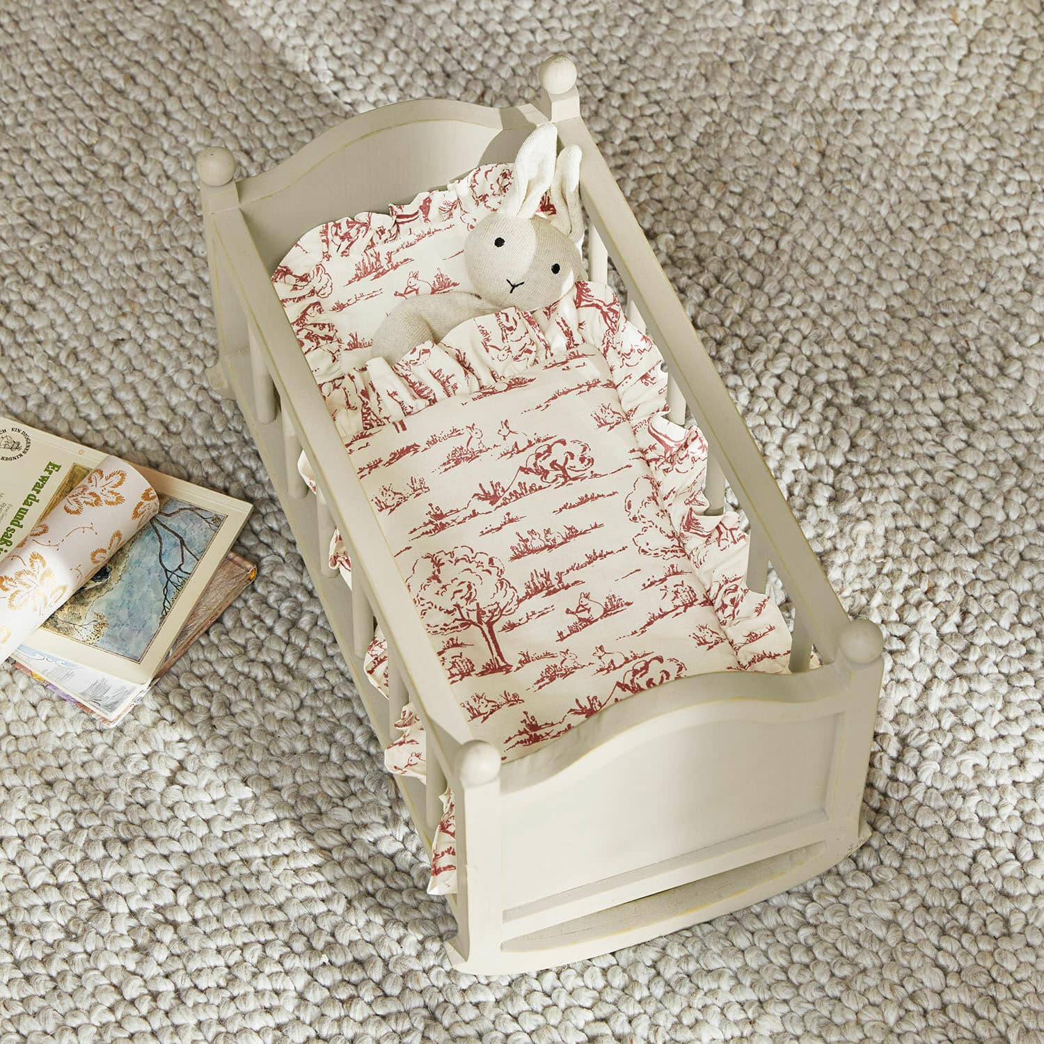 Cuna de muñecas Erilea Cama de madera para muñecas crema con ropa de cama estampada roja y conejo de peluche sobre alfombra gris