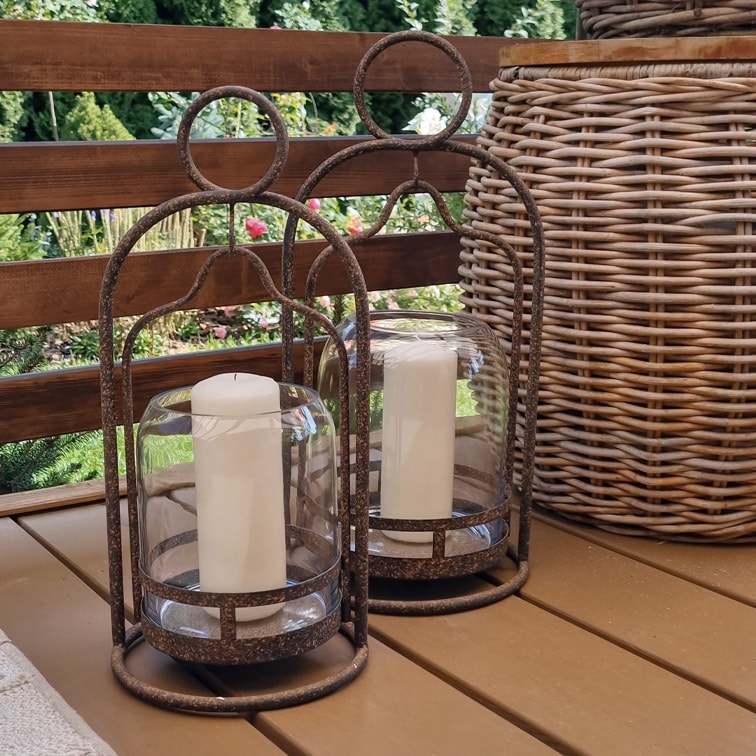 Dos faroles decorativos de metal con velas blancas sobre una mesa de madera en un jardín
