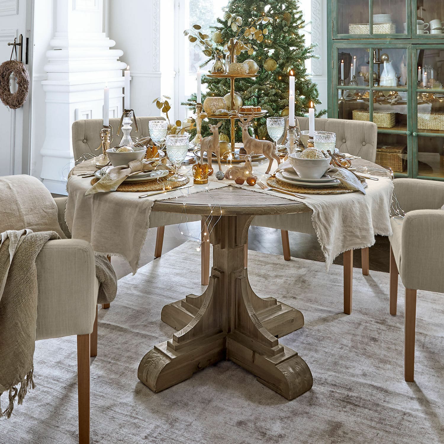 Mesa de comedor de madera con mantel beige y decoración navideña en tonos naturales y dorados