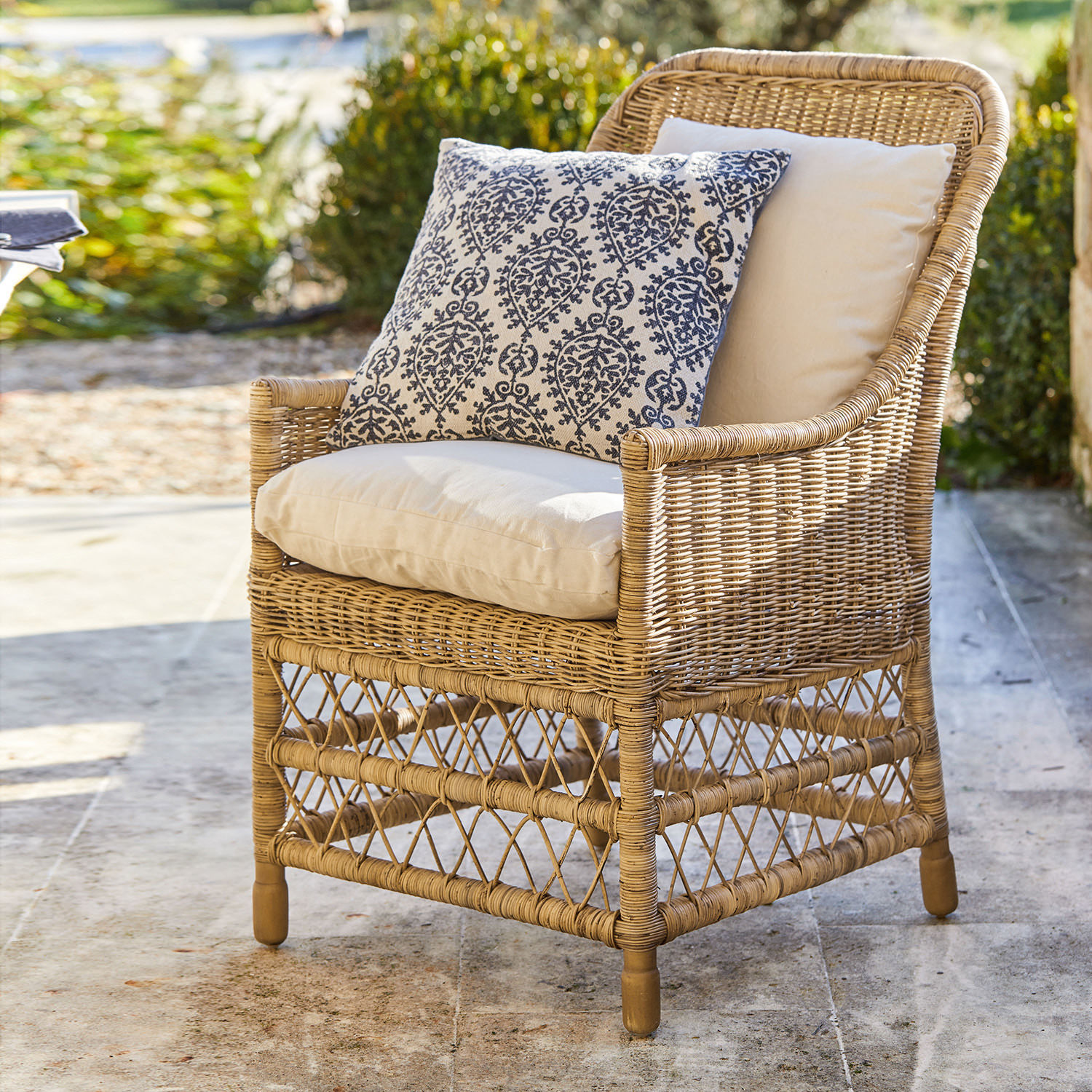 Sillón de ratán con cojines crema y cojín decorativo azul marino, mueble de jardín elegante