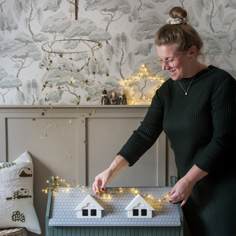 Mujer decorando un baúl de madera gris con luces LED en forma de estrellas en un ambiente acogedor