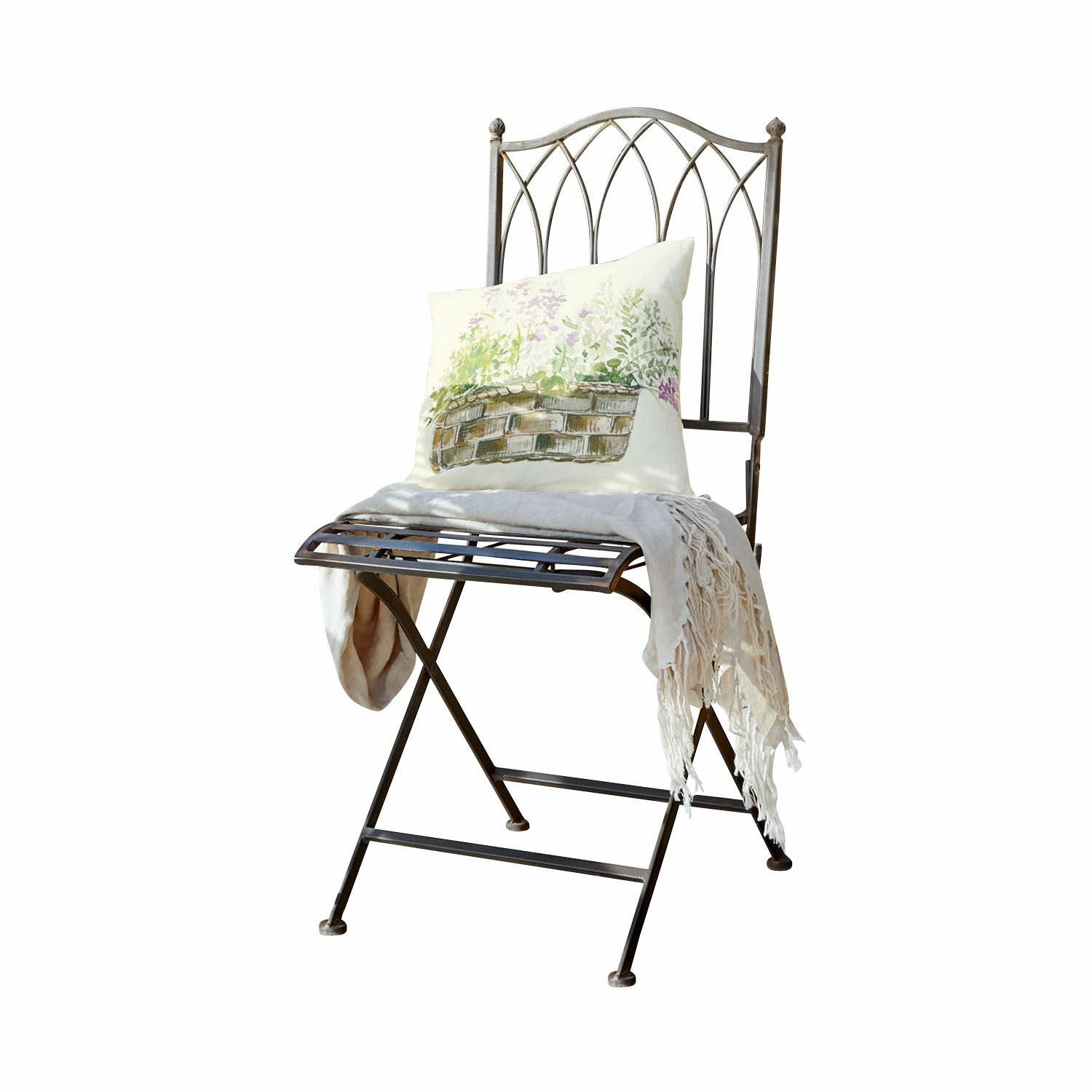 Silla de metal con respaldo decorativo, cojín claro con estampado y manta crema con flecos