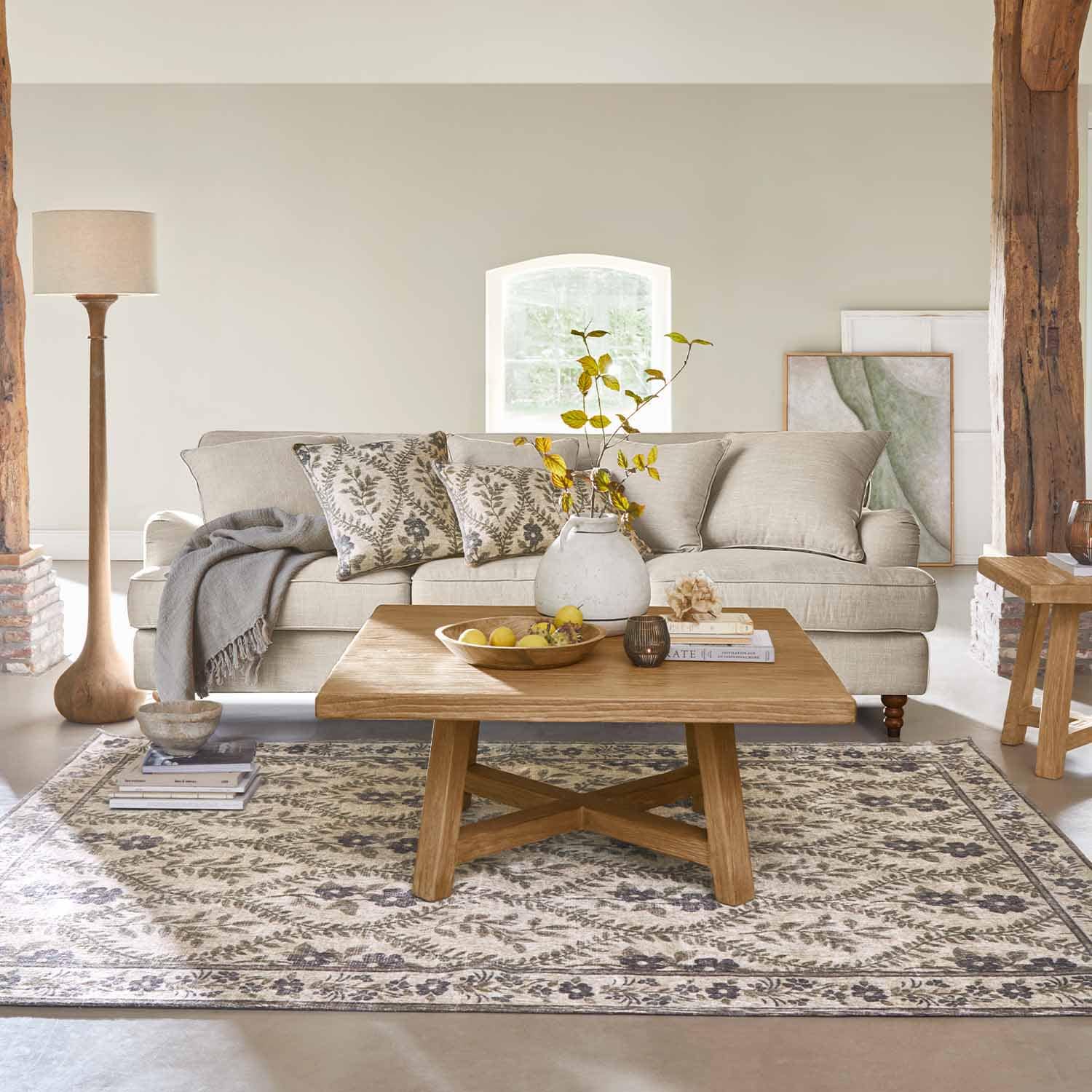 Sofá beige de tela con cojines decorativos y mesa de centro de madera sobre alfombra estampada