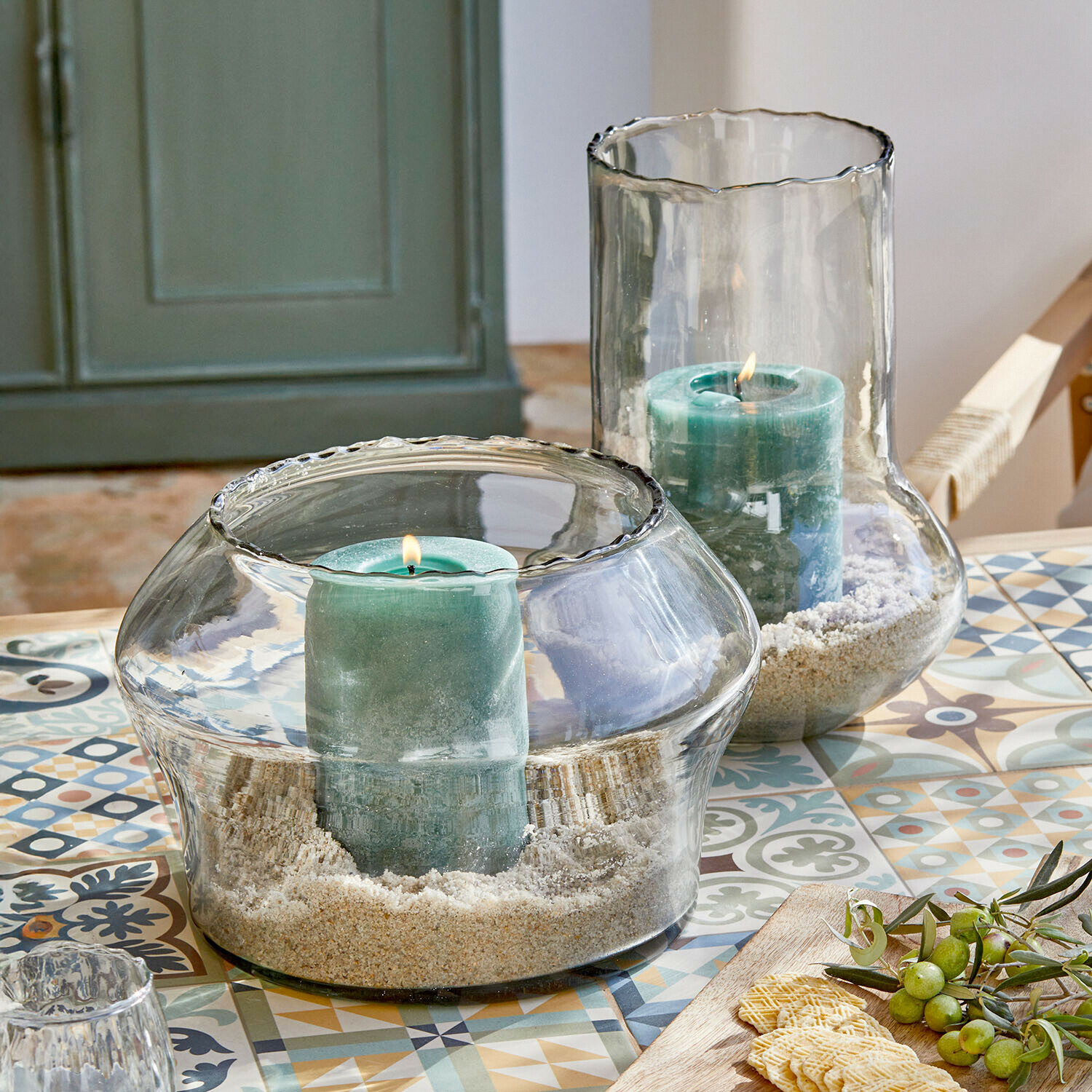 Set de 2 portavelas Lumiras Portavelas de vidrio con velas verdes y arena sobre mesa colorida con patrones decorativos