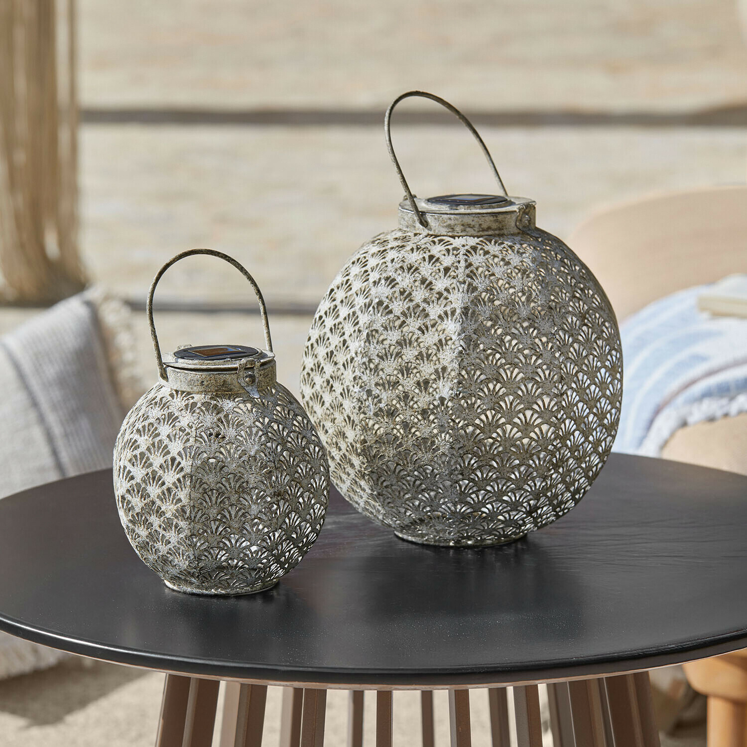 Set de 2 farolillos solares Omirah Dos faroles de metal calado gris sobre mesa negra, decoración para exteriores elegante