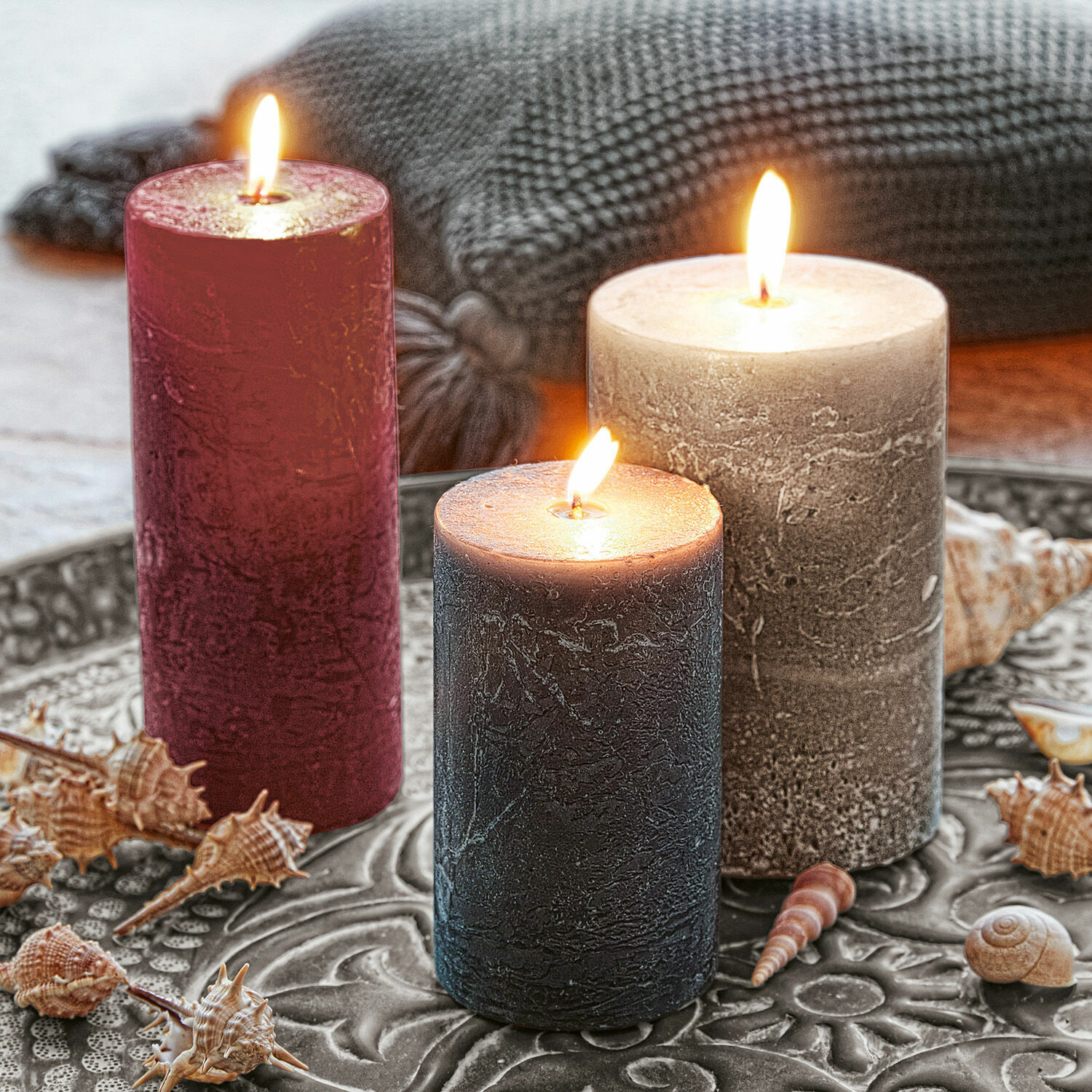 Set de 3 velas Pretin Tres velas decorativas en rojo, gris y negro sobre una bandeja metálica con conchas marinas