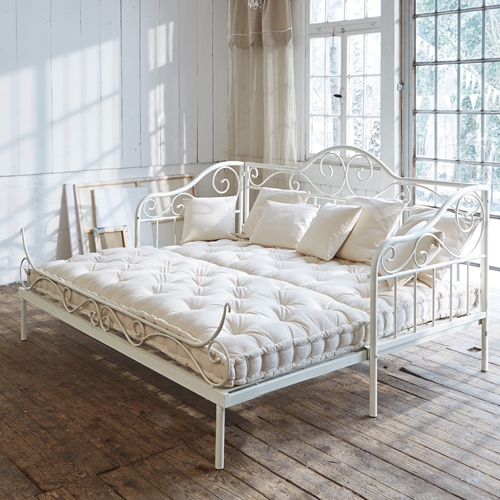 Sofá metálico blanco con colchón crema y cojines en habitación luminosa con suelo de madera
