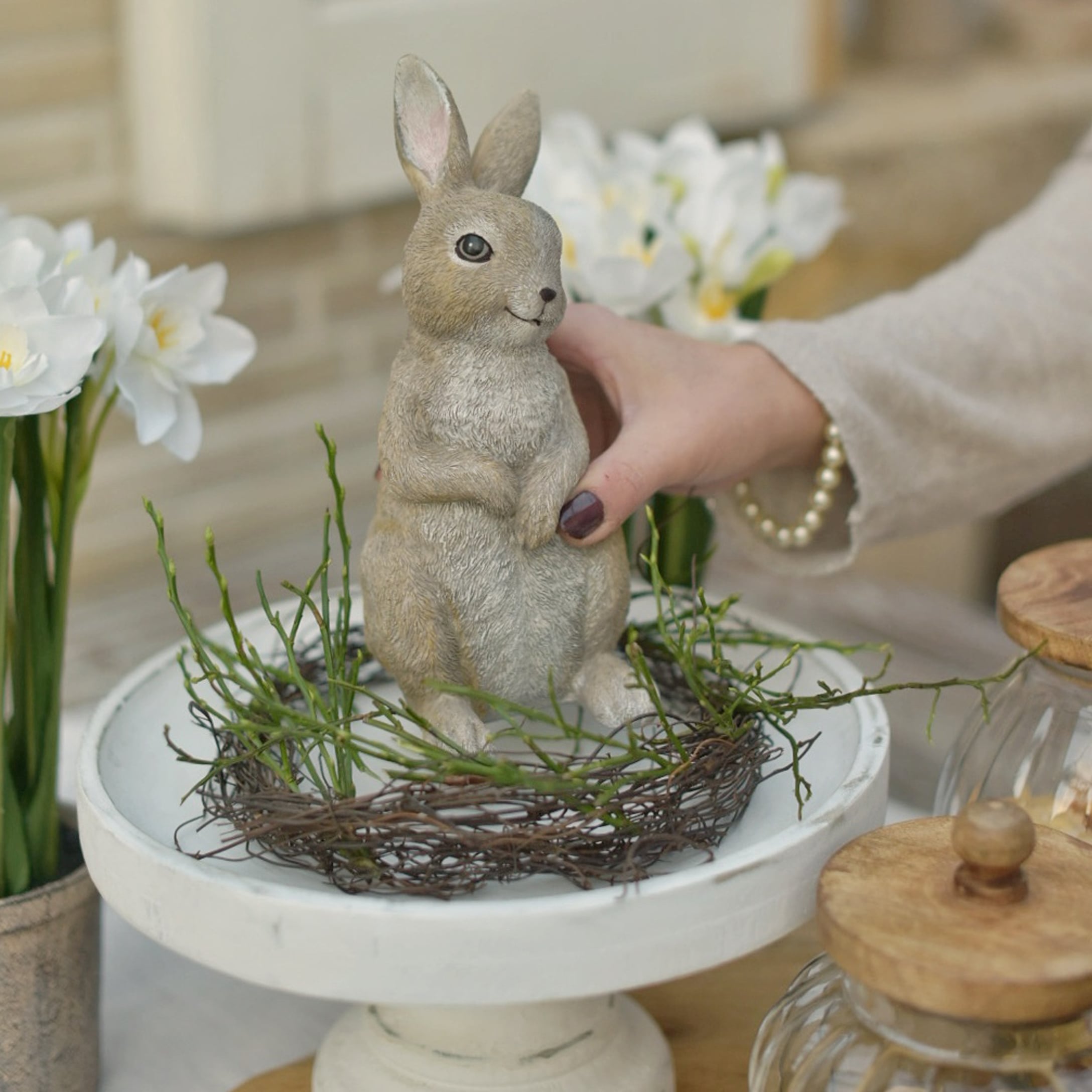 Conejo decorativo de Pascua en colores naturales sobre base blanca con ramas verdes