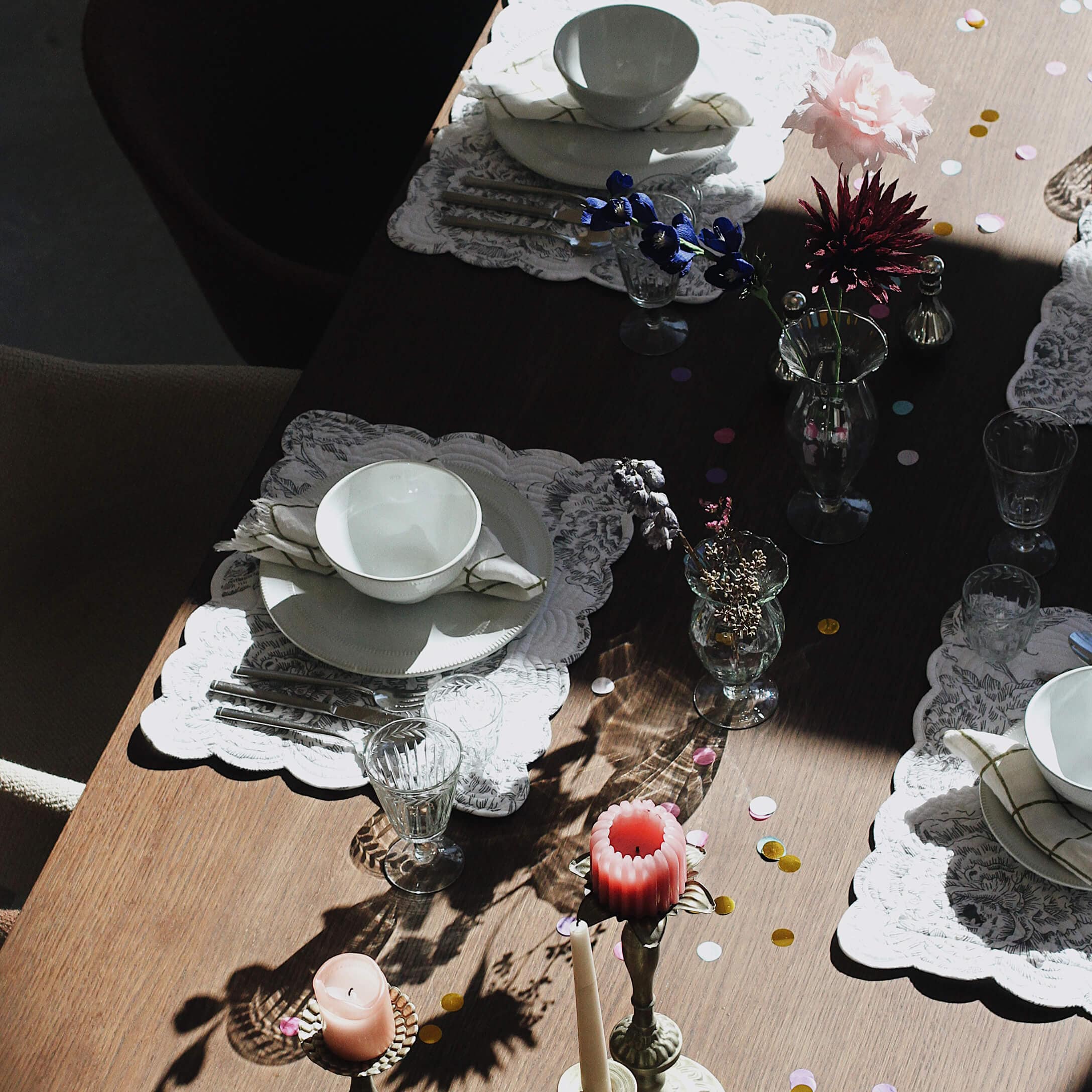 Mesa elegantemente puesta con vajilla blanca, vasos y velas sobre superficie de madera