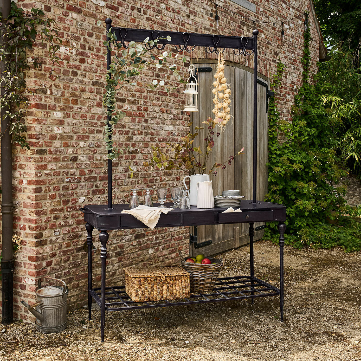 Estante Langmore Mesa de jardín de metal negro con ganchos y estante, decorada con jarras y cesta de frutas