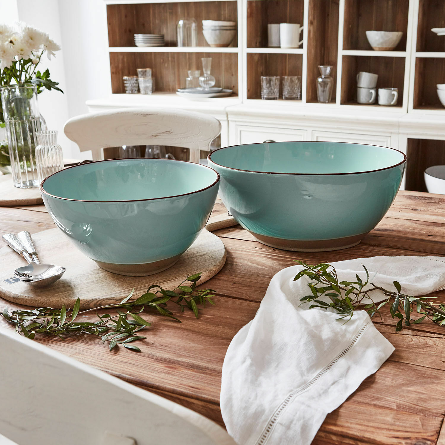 Set de 2 ensaladeras Biarré Conjunto de dos cuencos de cerámica turquesa sobre mesa de madera con decoración de ramas verdes