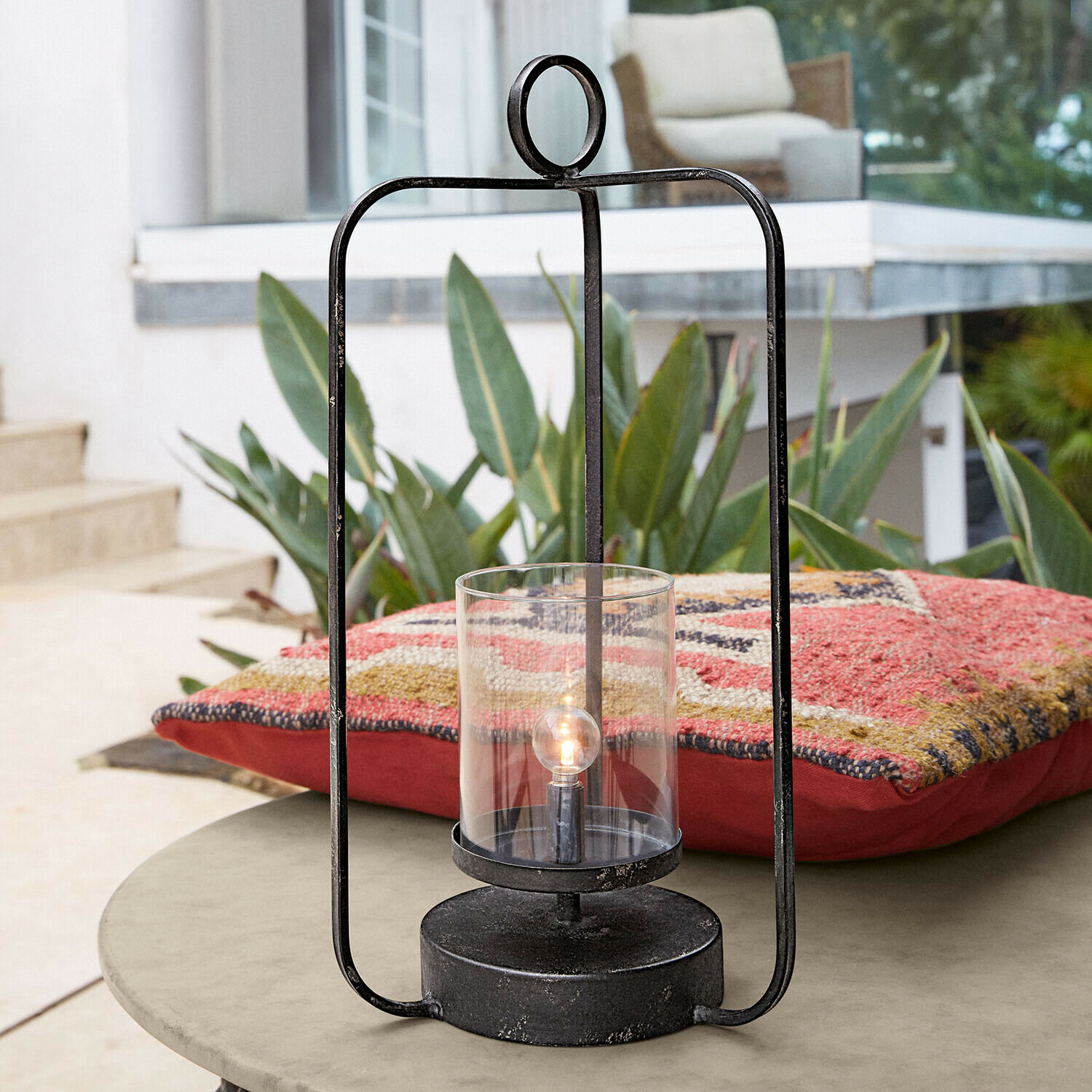 Farolillo LED Kivalex Linterna negra de metal con vidrio transparente sobre mesa de jardín con cojín colorido