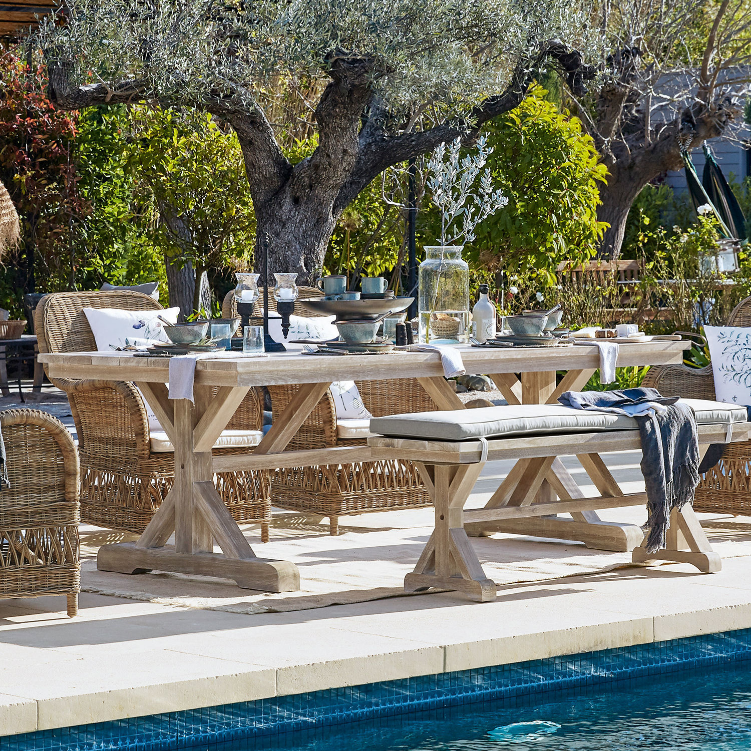 Mesa FSC®-100% Graslin Mesa de jardín de madera clara con sillas de mimbre junto a la piscina en entorno natural al aire libre