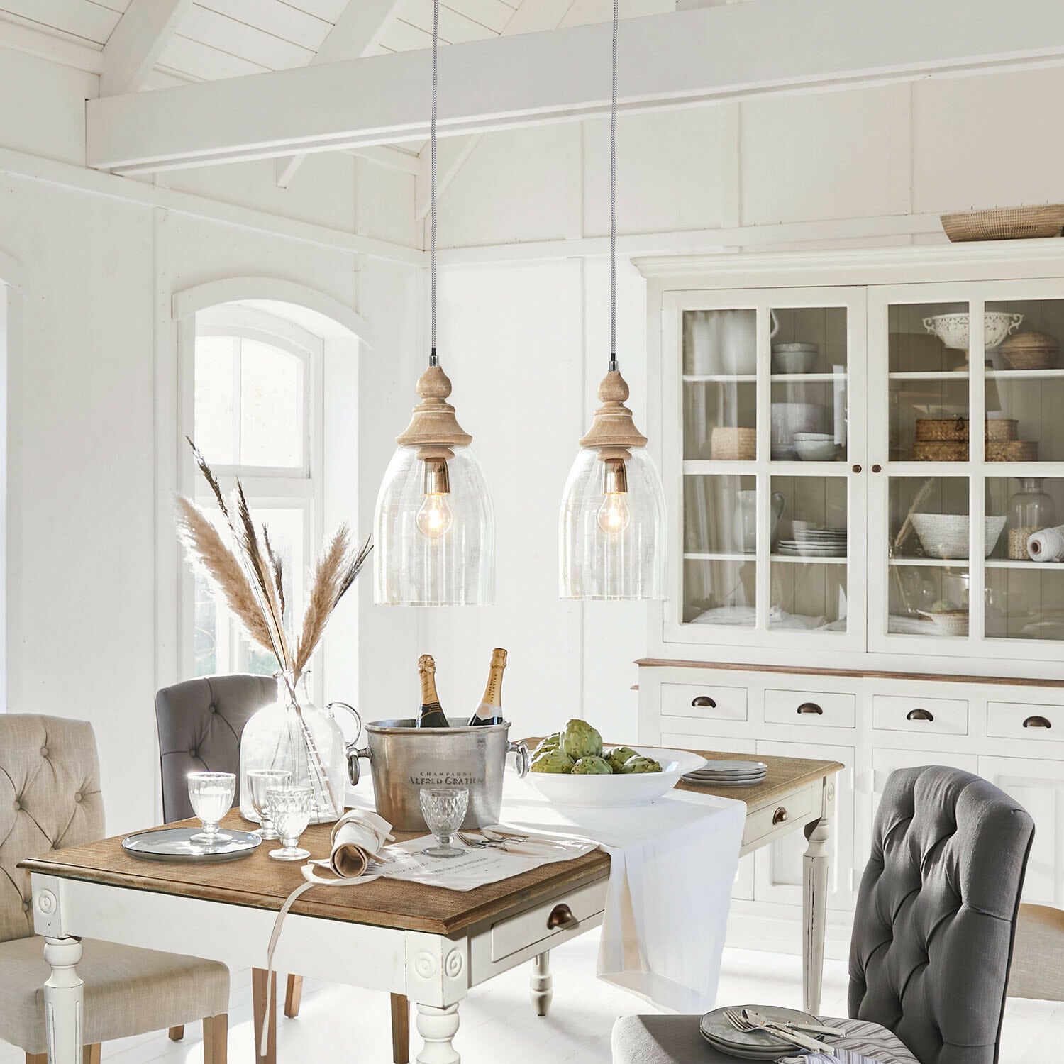 Comedor rústico con mesa de madera blanca, sillas tapizadas grises y vitrina con decoración de mimbre