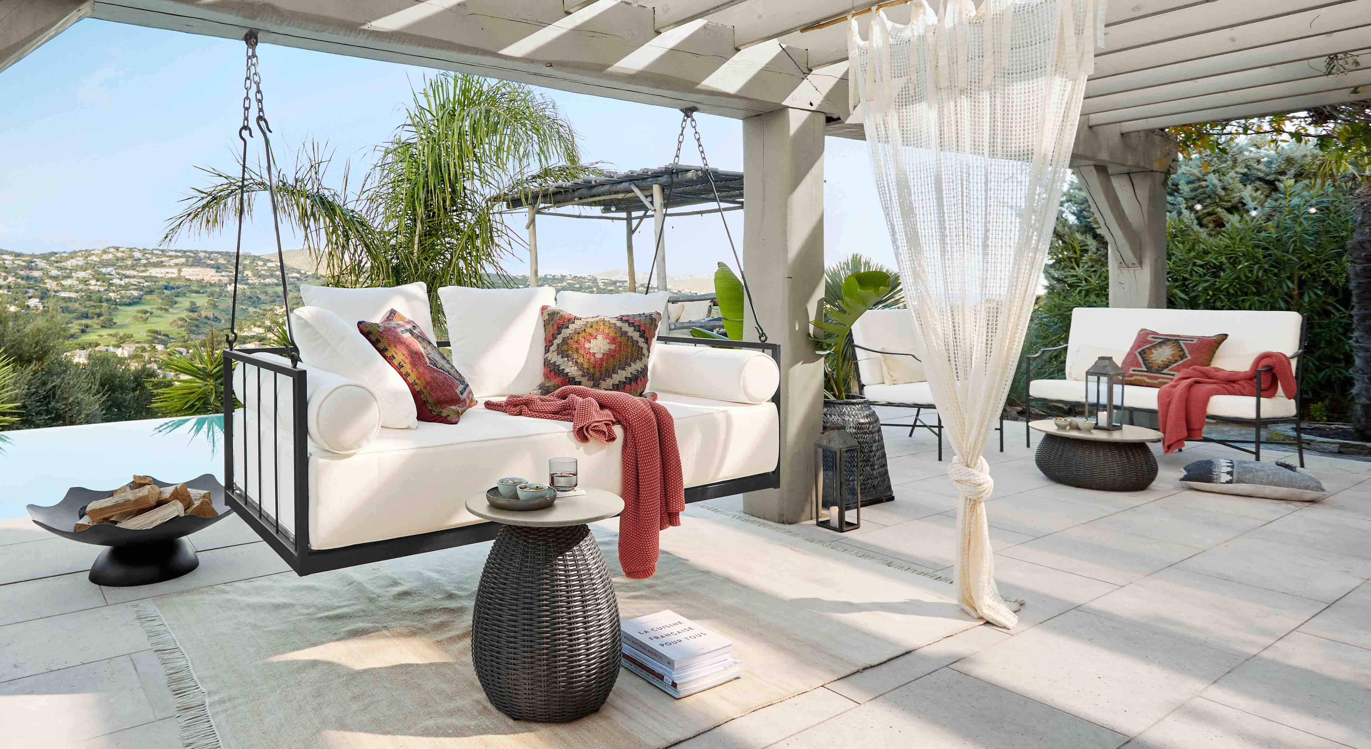 Sofá colgante blanco con estructura metálica y cojines coloridos en terraza con vistas a colinas