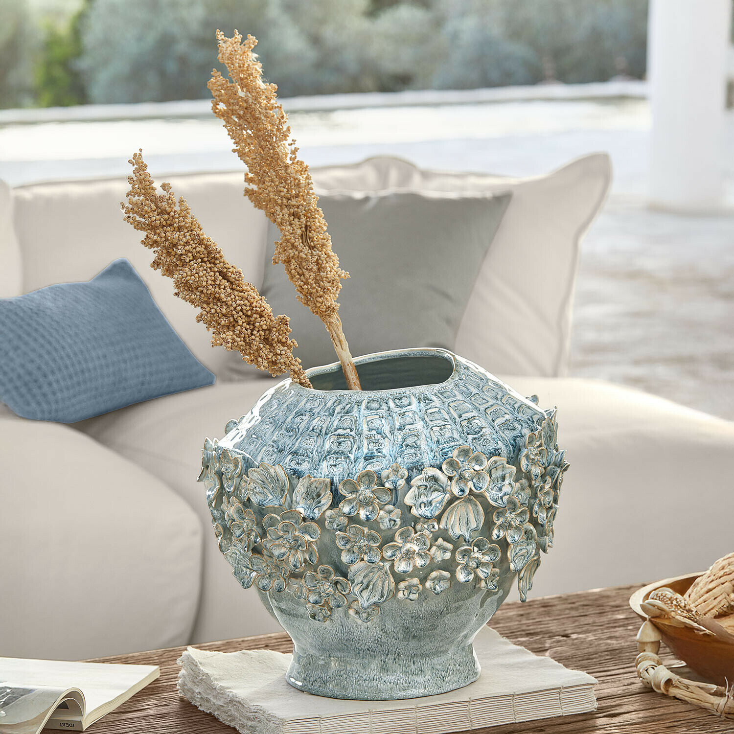 Jarrón decorativo de cerámica azul con relieve floral sobre mesa de madera en sala luminosa