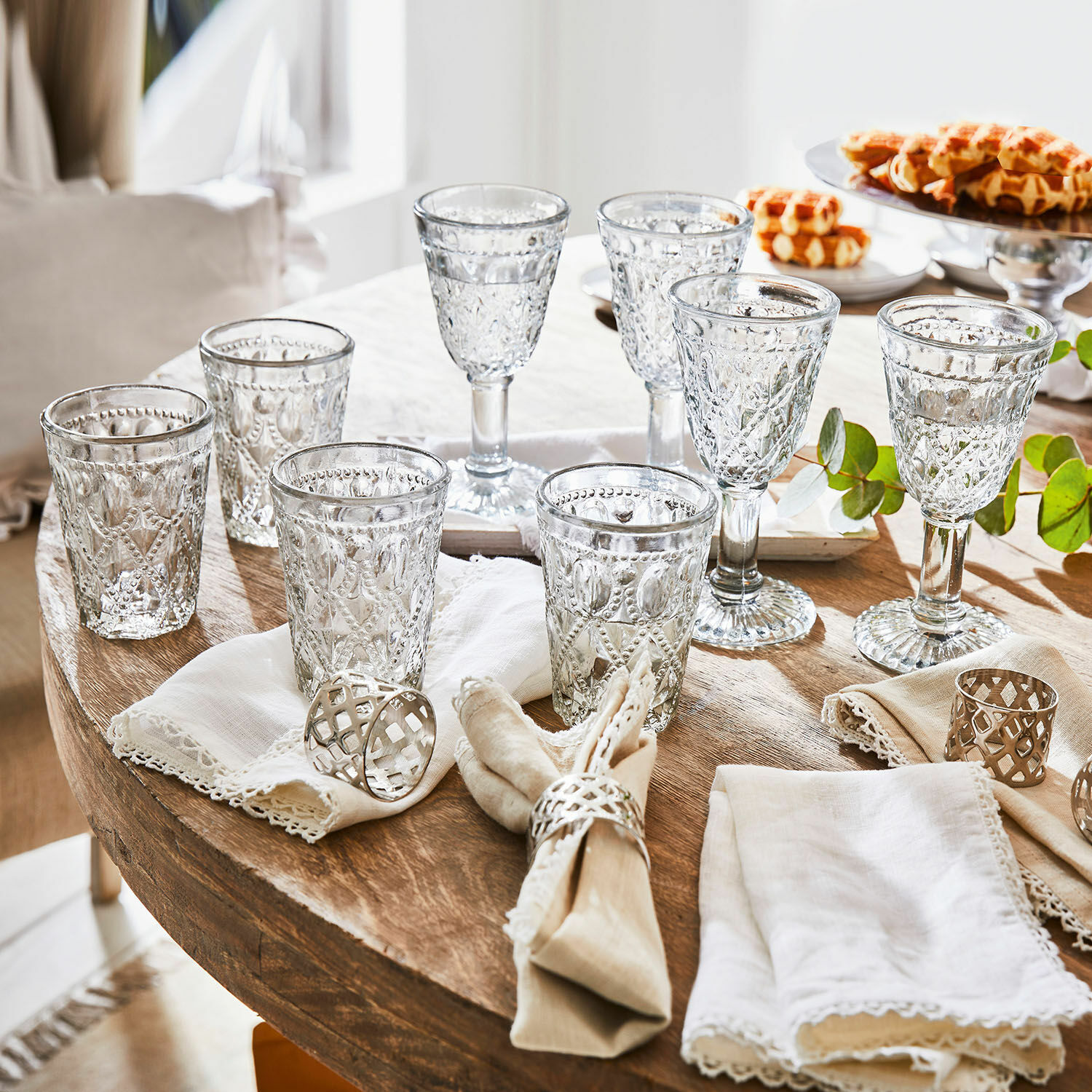 Set de 8 vasos Vérane Conjunto de vasos y copas de vidrio transparente con diseño decorativo sobre mesa de madera con servilletas