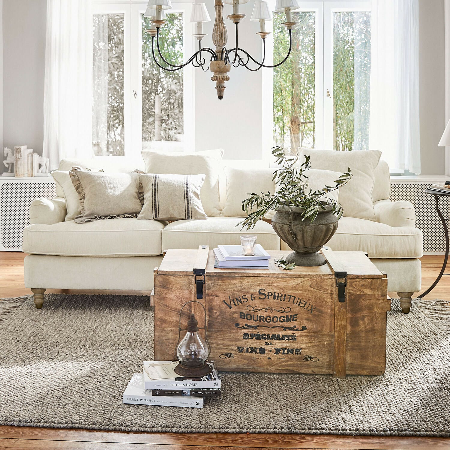Sofá Isa Baúl de madera con texto vintage como mesa de centro en salón luminoso con sofá beige y decoración