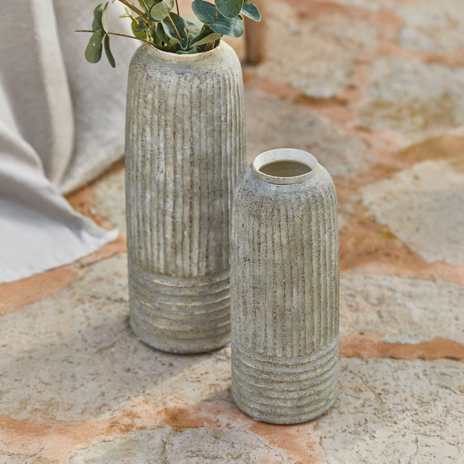 Dos jarrones de cerámica gris con ranuras verticales sobre suelo de piedra, decoración para interiores