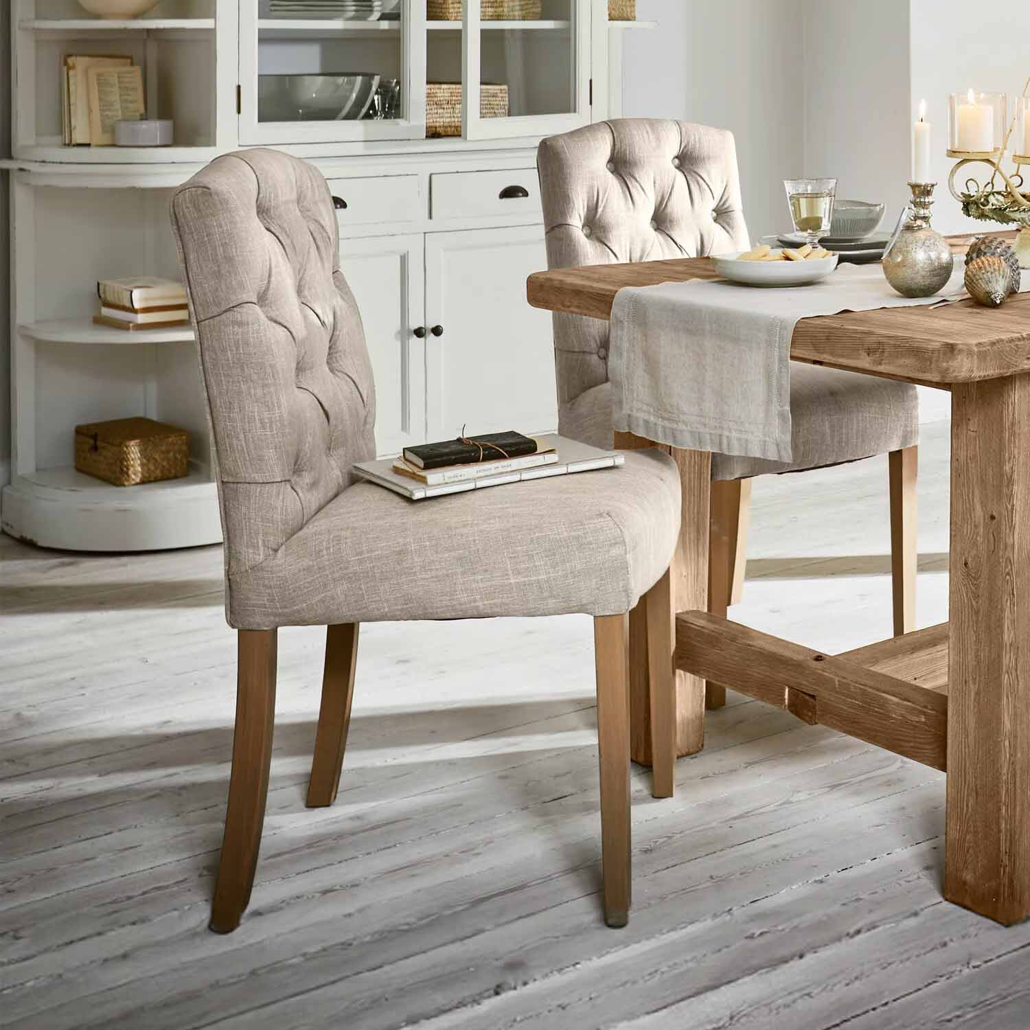 Silla tapizada beige con patas de madera junto a mesa de madera en comedor luminoso
