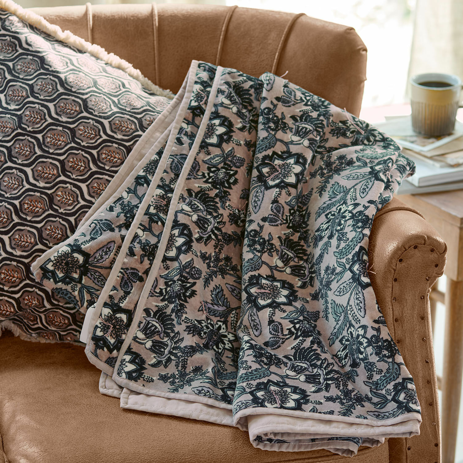 Plaid Elarion Manta suave con diseño floral gris sobre sofá beige con cojín decorativo estampado
