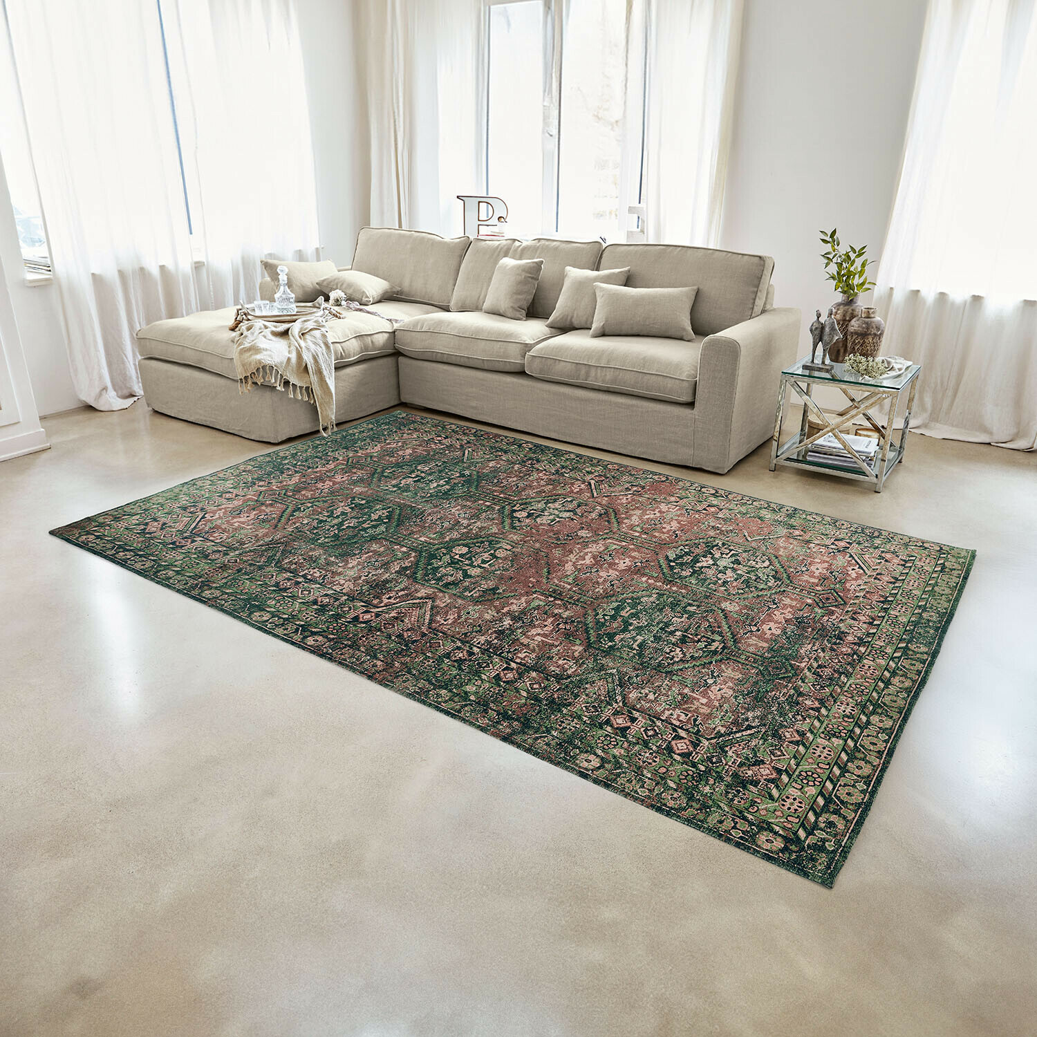 Alfombra Incantaro Alfombra con diseño oriental en tonos verdes y rosas sobre suelo claro en salón moderno con sofá beige