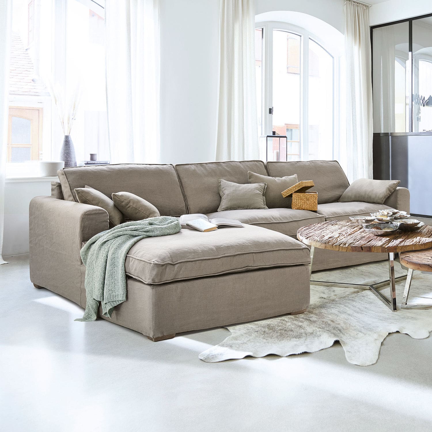 Sofá Seaford Sofá rinconero beige de tela en sala luminosa con mesa de madera y decoraciones