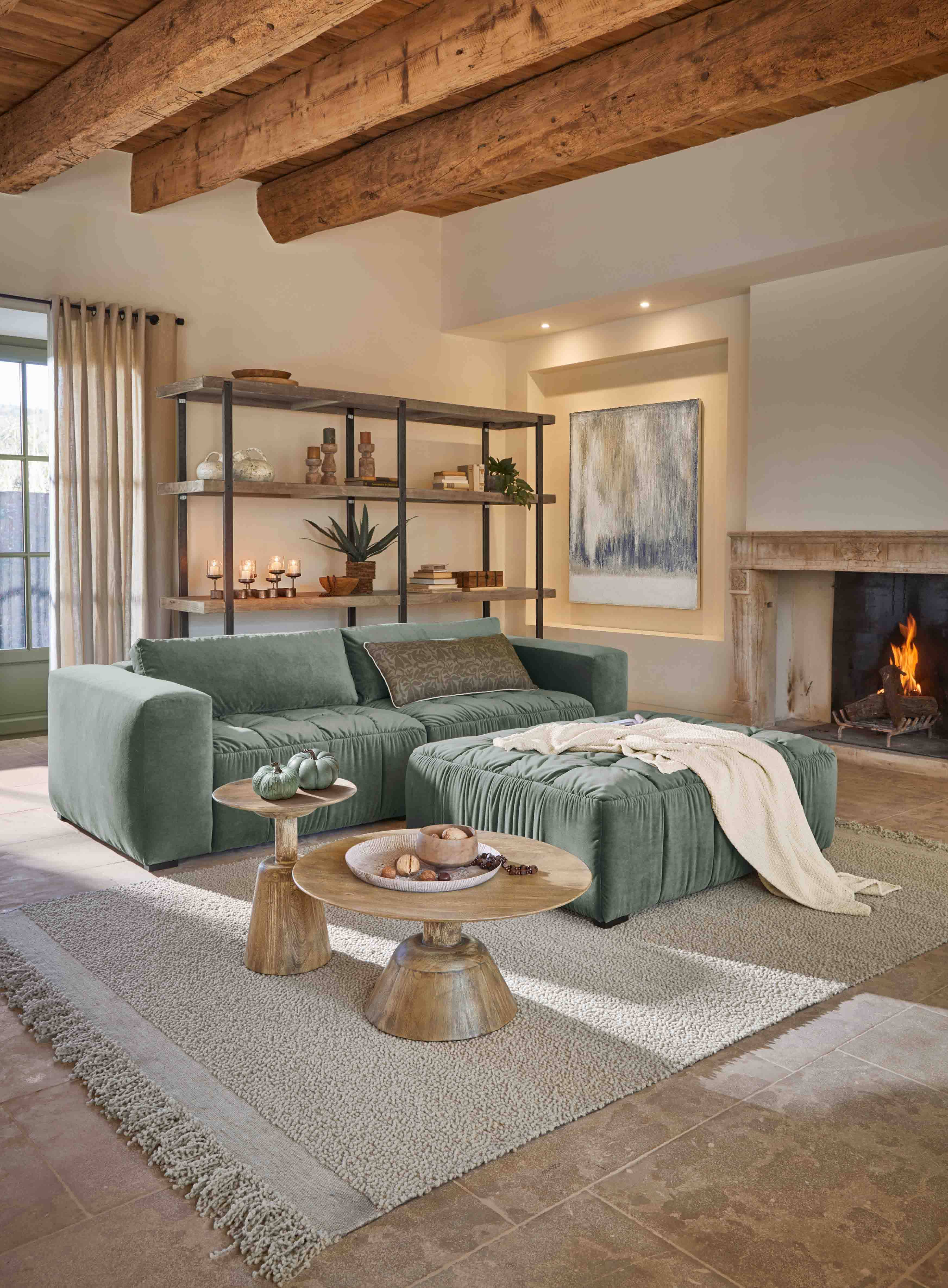 Sala acogedora con sofá verde de terciopelo, puf a juego, mesas de madera y chimenea encendida