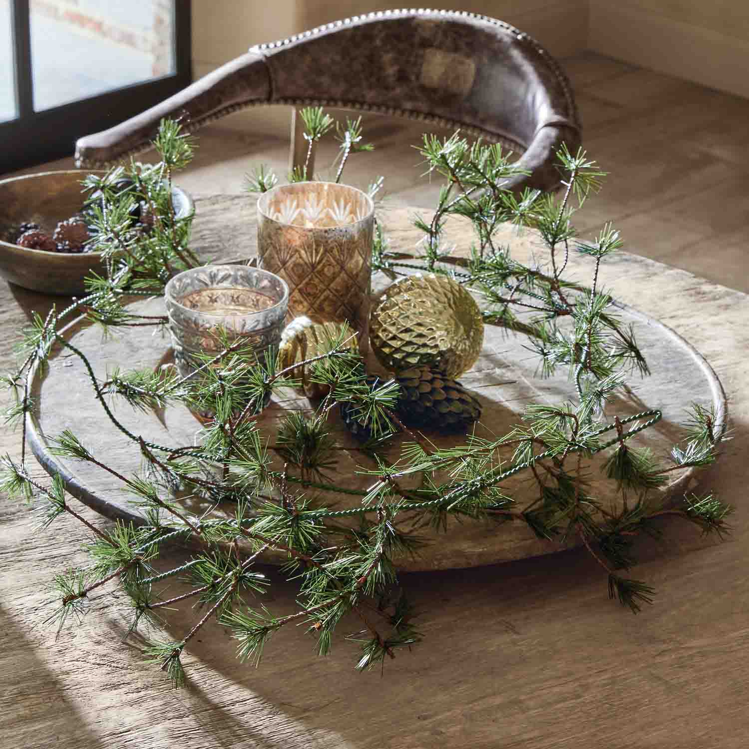 Bandeja de madera decorativa con ramas verdes, adornos dorados y portavelas de vidrio sobre mesa
