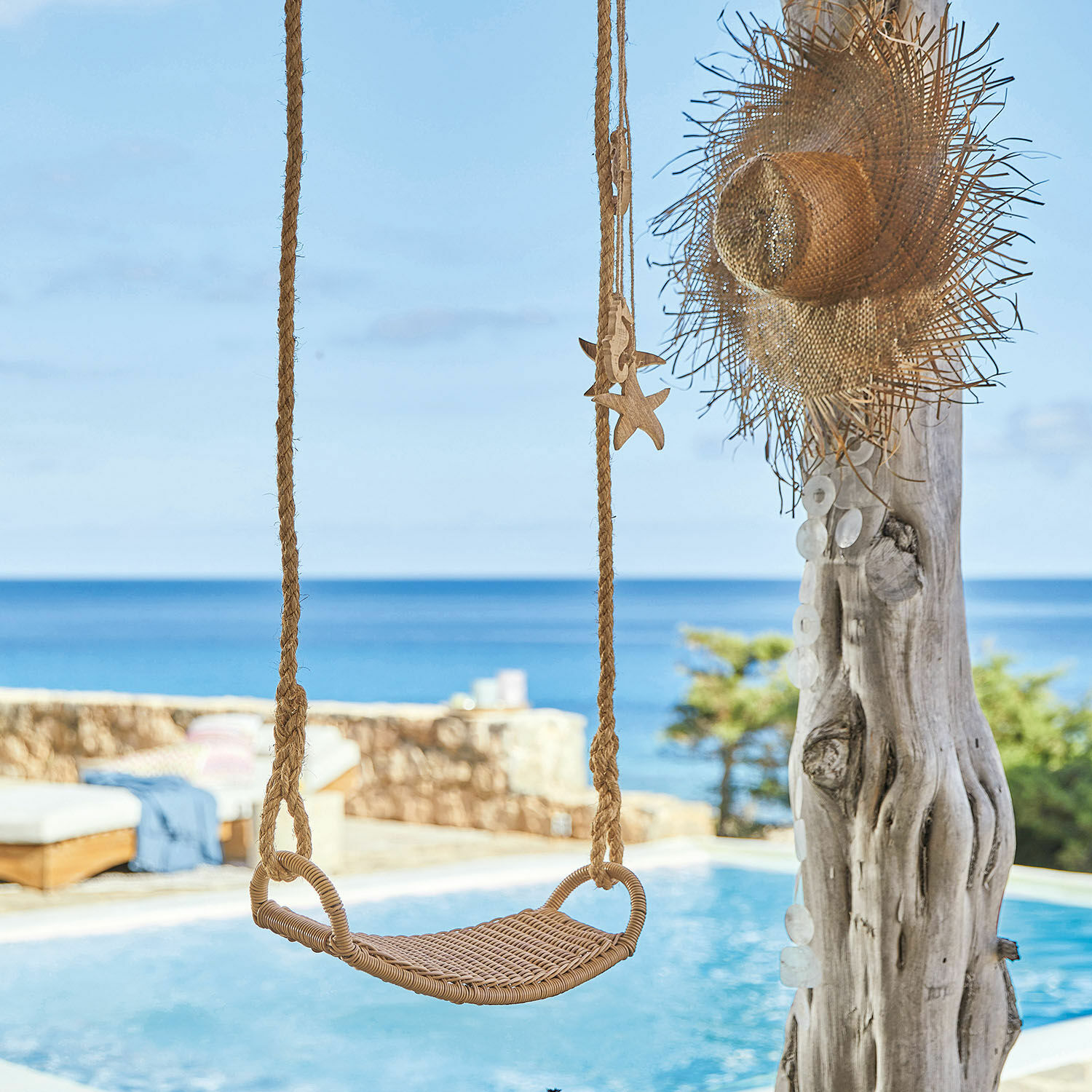 Columpio de ratán color natural frente a piscina y mar, decoración veraniega para jardín