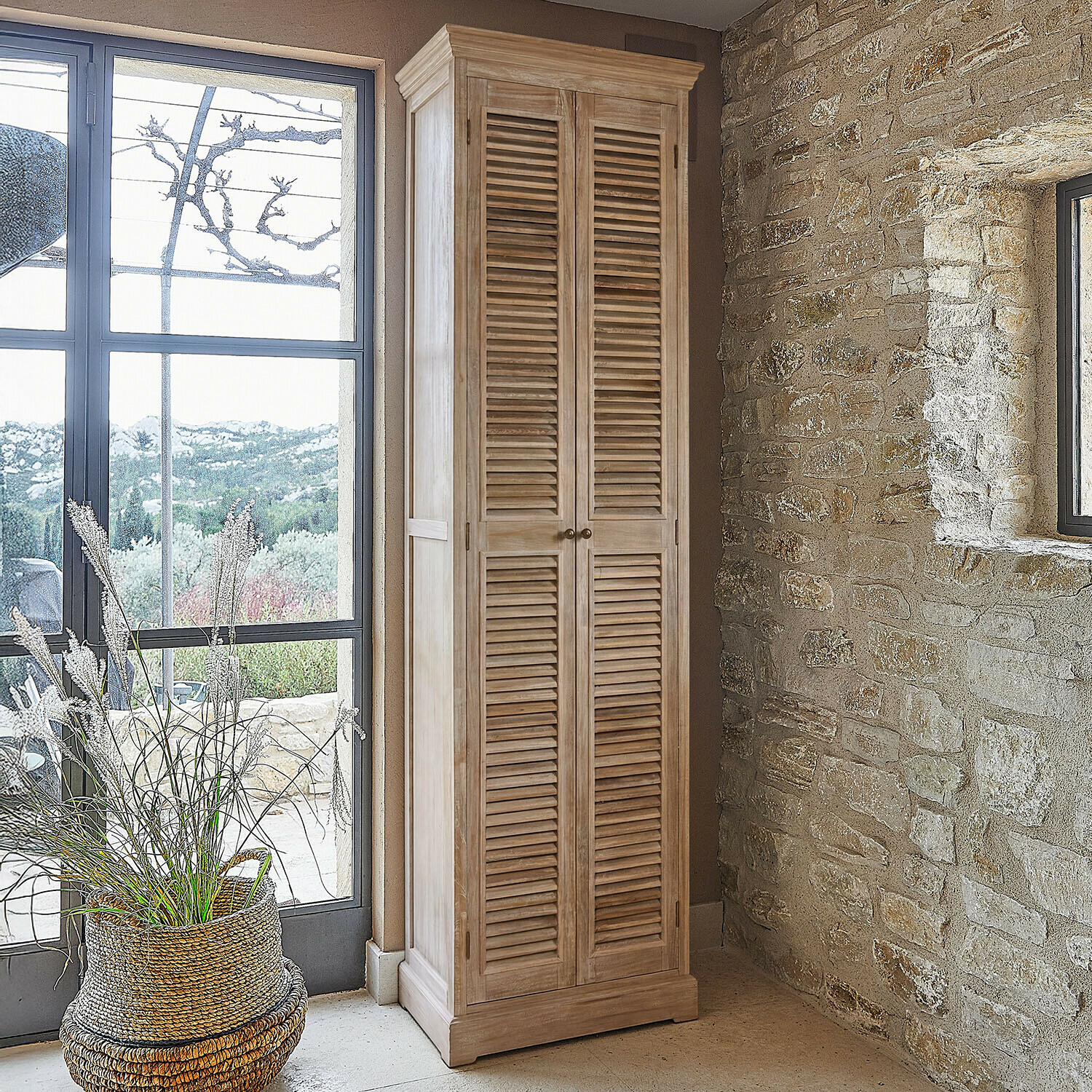 Armario alto de madera natural con puertas de persiana en interior rústico con pared de piedra