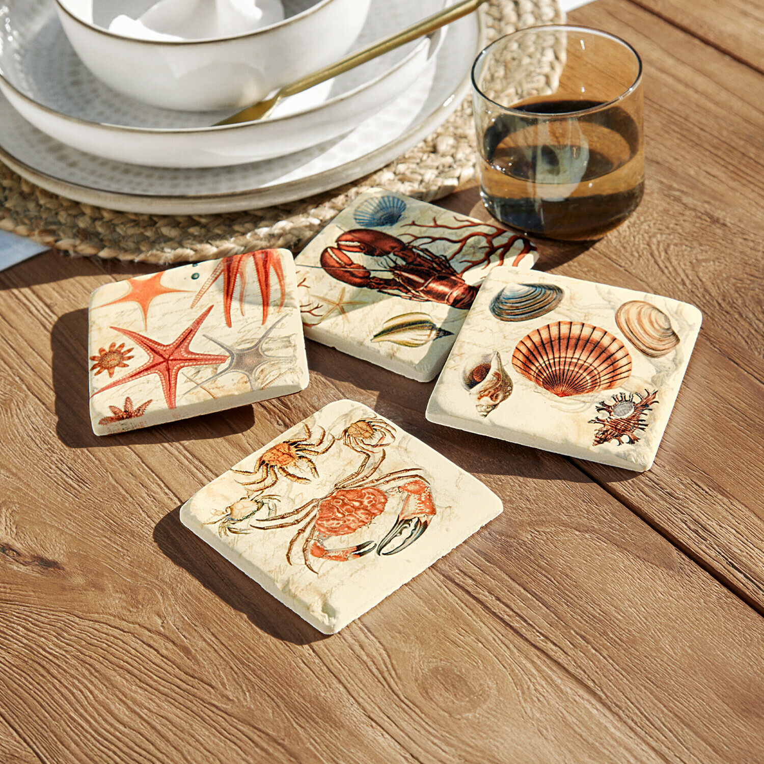 Set de 4 posavasos Celorin Conjunto de cuatro posavasos de cerámica con motivos marinos en colores cálidos sobre mesa de madera