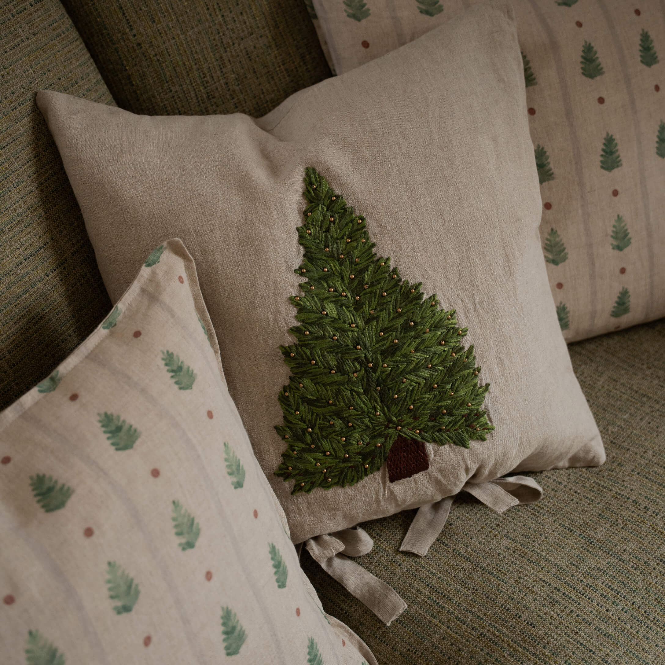 Cojín de lino beige con árbol verde bordado y cuentas decorativas sobre sofá texturizado