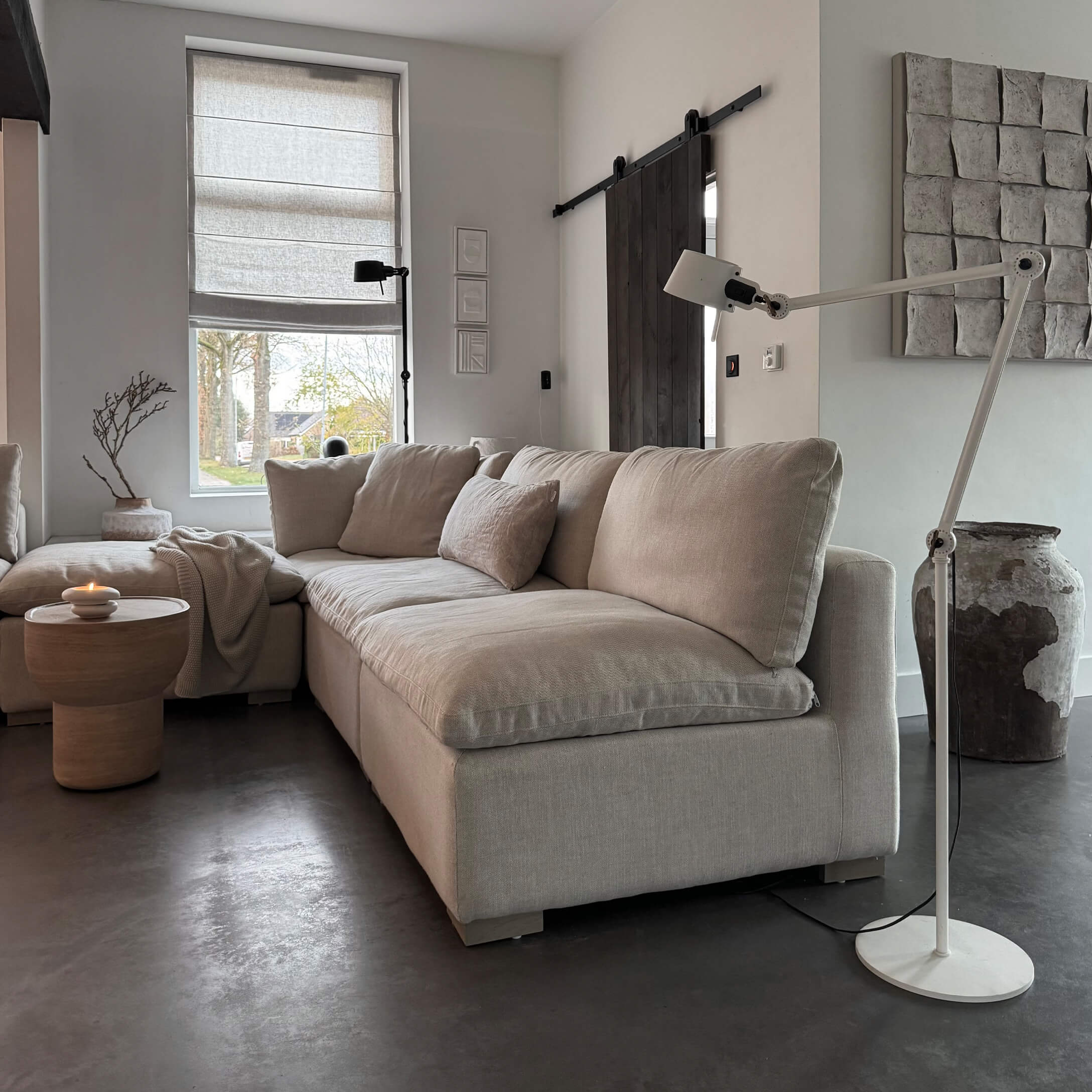 Sofá esquinero beige de tela en salón moderno con lámpara de pie y mesa auxiliar de madera