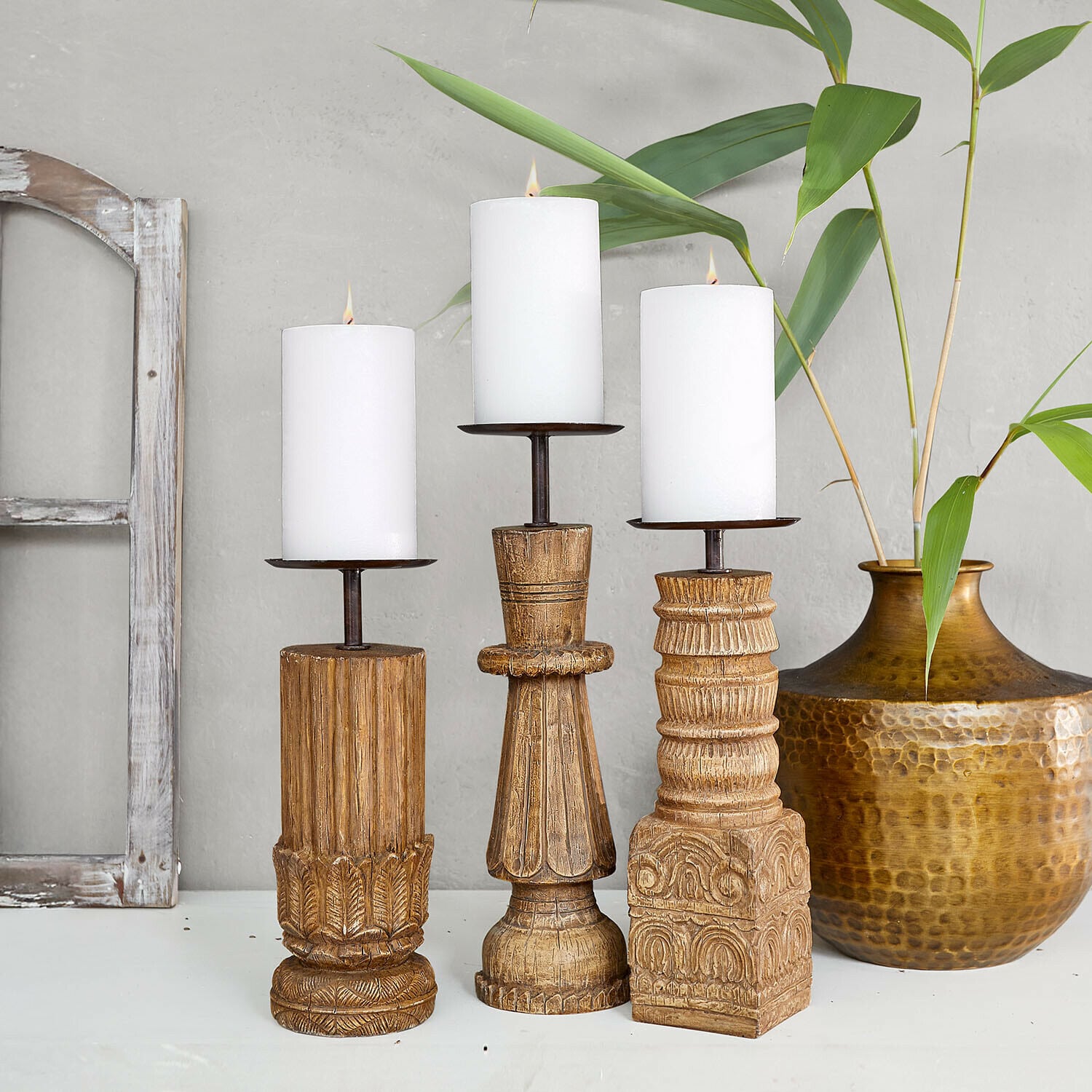 Set de 3 candeleros Zahirah Conjunto de tres candelabros de madera tallada con velas blancas, color natural y diseño decorativo