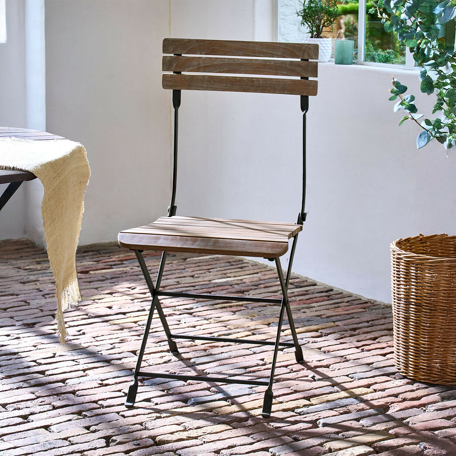 Silla Arémont Silla plegable de madera con estructura metálica negra sobre suelo de ladrillo con luz natural