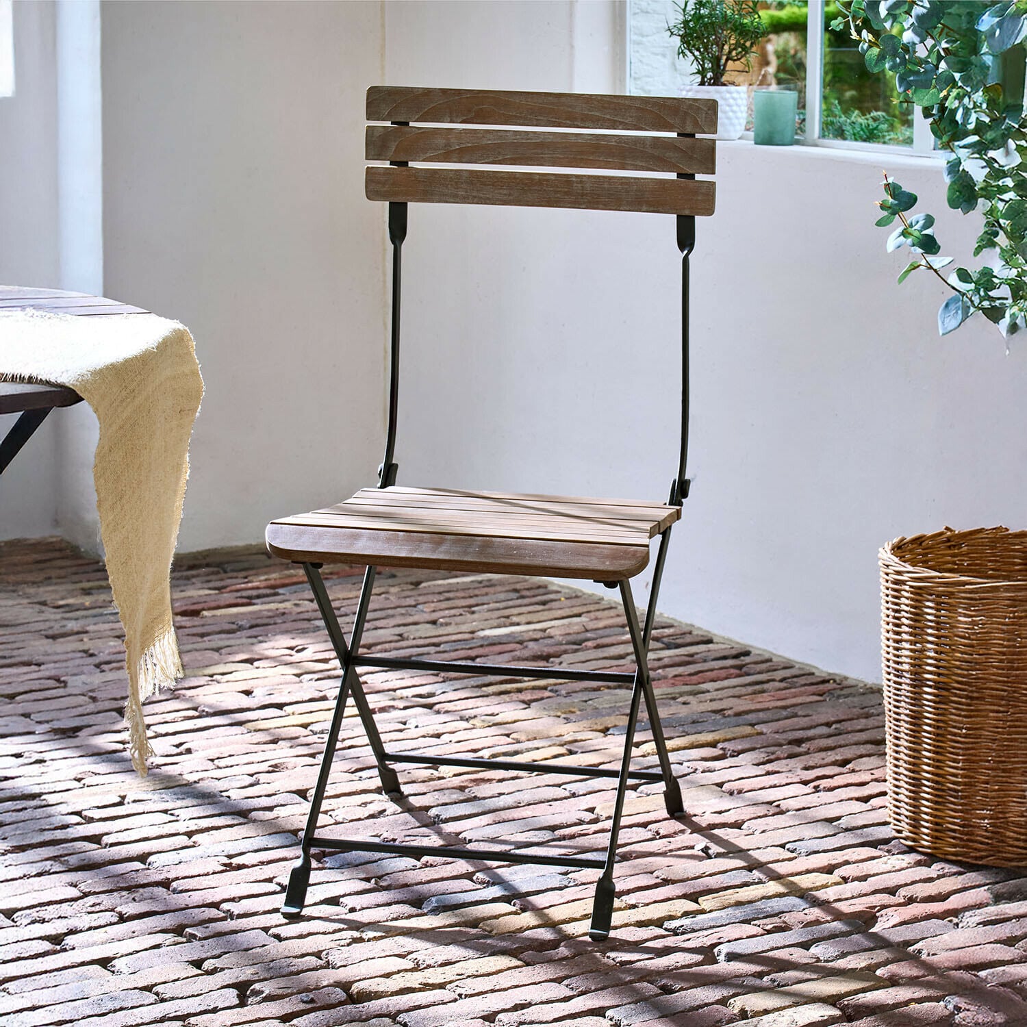 Silla Arémont Silla plegable de madera con estructura metálica negra sobre suelo de ladrillo con luz natural