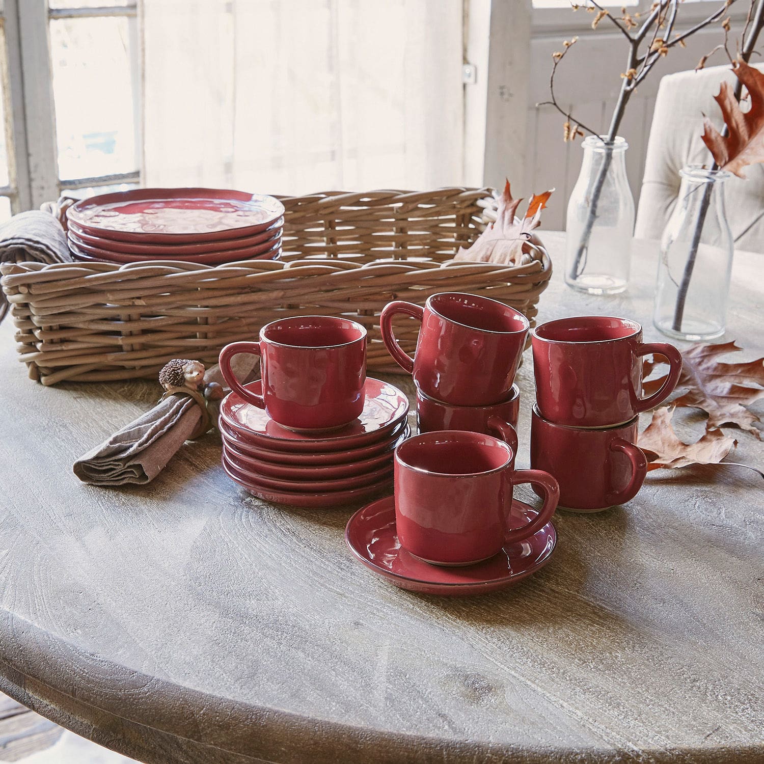 Set de 6 tazas y platillos Biarré Juego de tazas y platos de cerámica roja sobre mesa de madera con cesta de mimbre