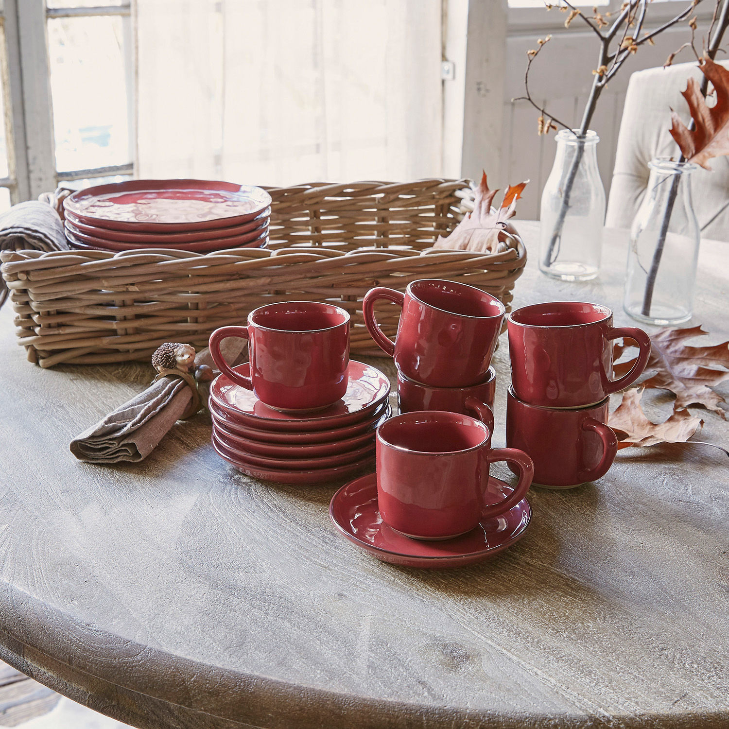Set de 6 tazas y platillos Biarré Juego de tazas y platos de cerámica roja sobre mesa de madera con cesta de mimbre