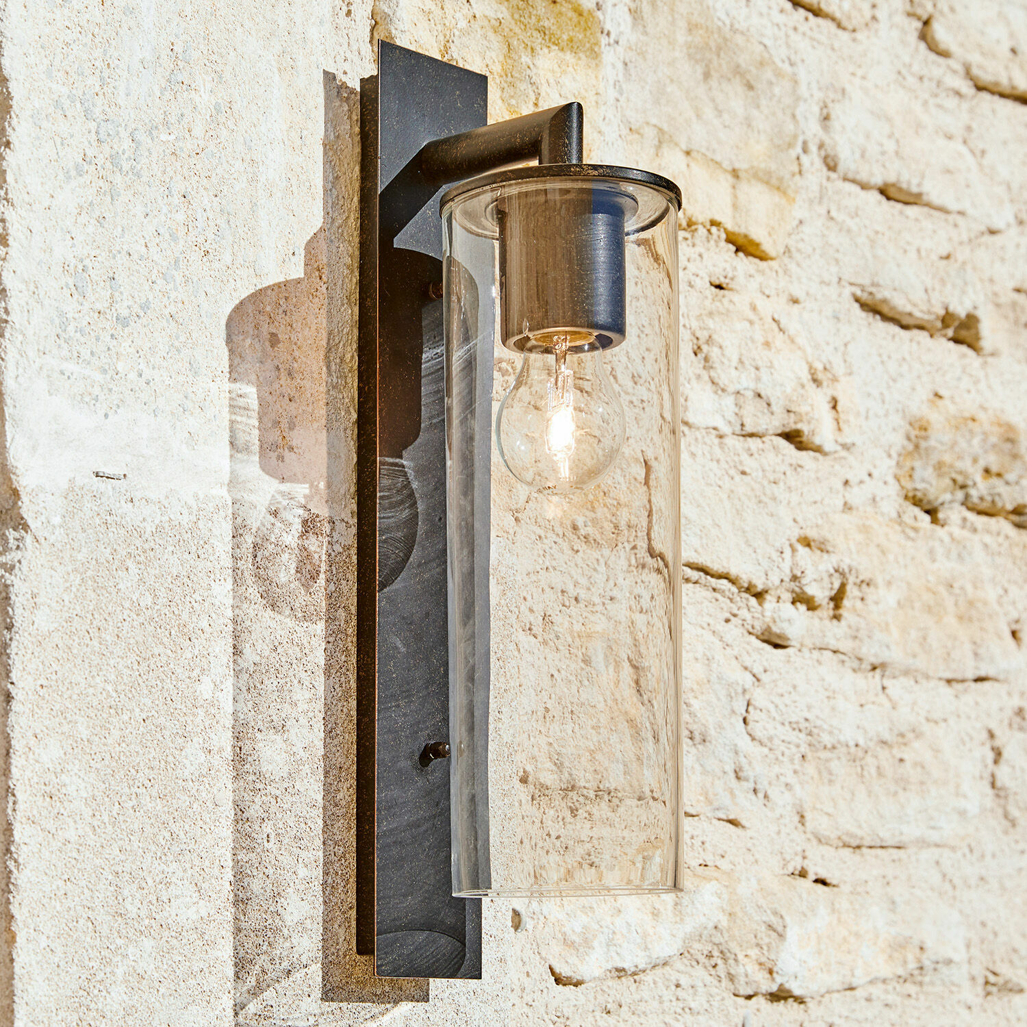 Aplique de exterior Clisson Lámpara de pared negra de metal con pantalla de vidrio transparente en pared de piedra clara