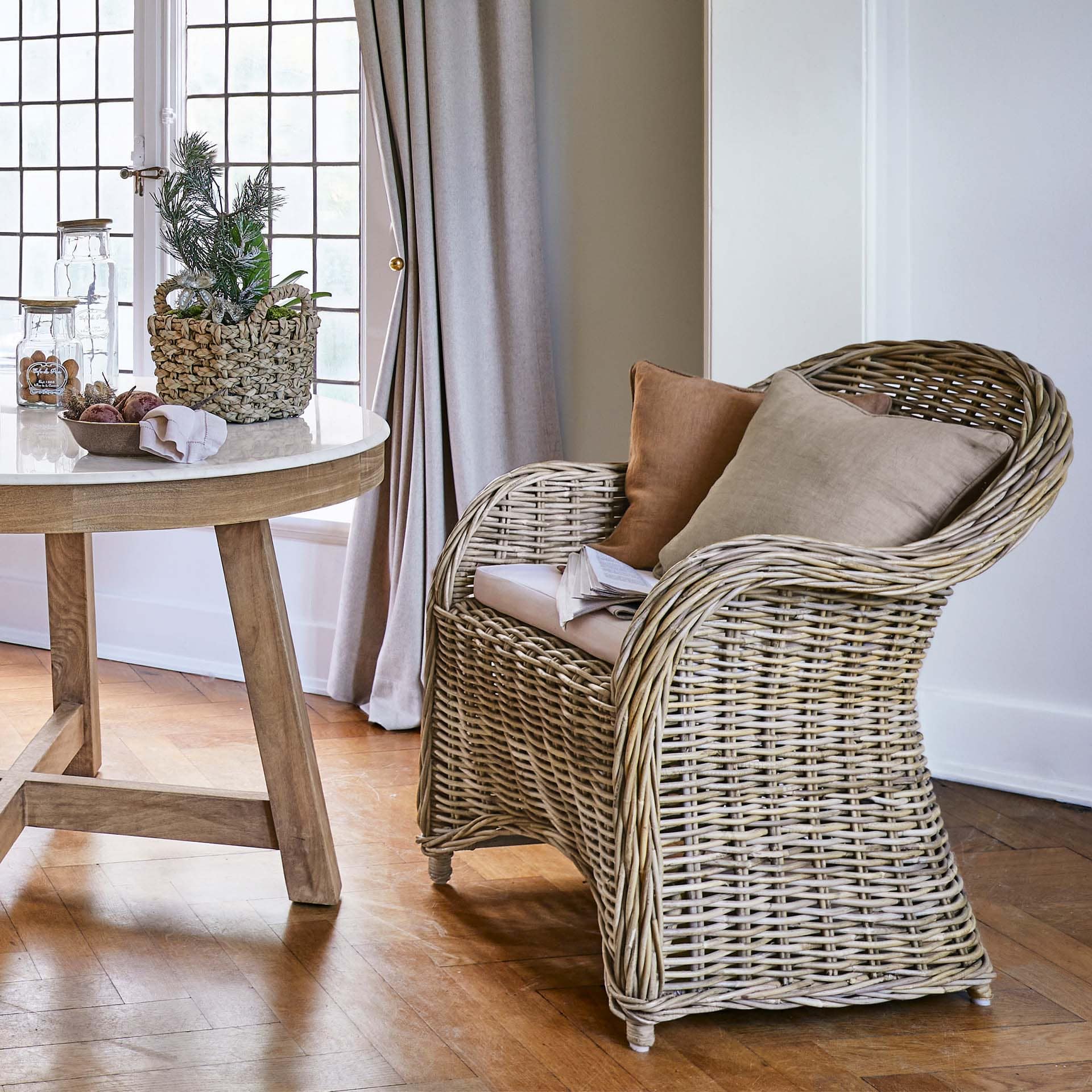 Sillón de ratán natural con cojines beige en salón luminoso con suelo de madera